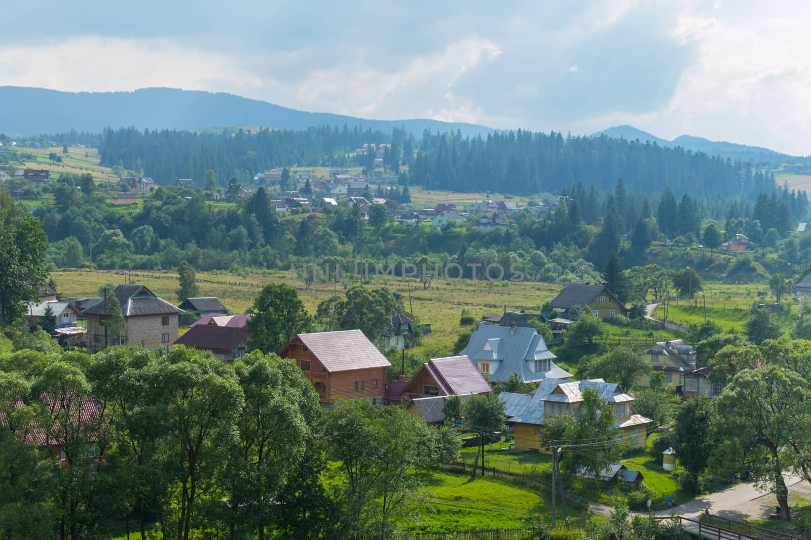 A beautiful and cozy village is located at the foot of the majestic mountains against the background of a misty sky