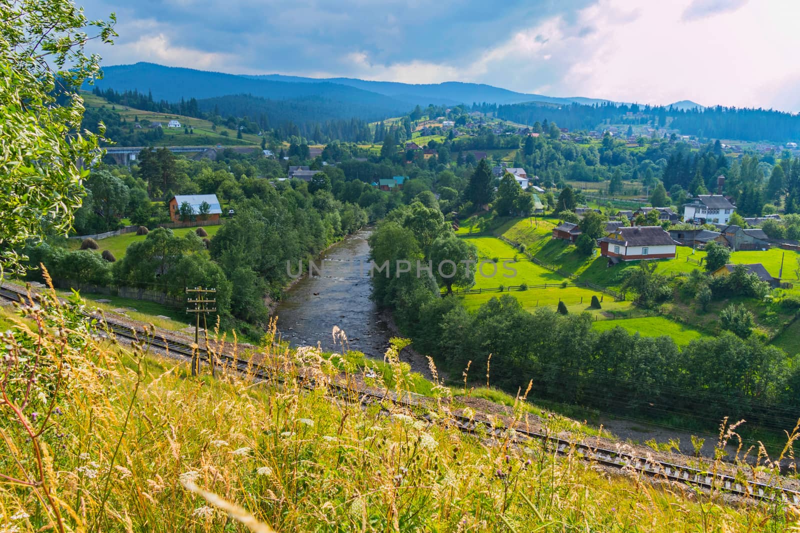 railway between the meadow and the river on the background of village