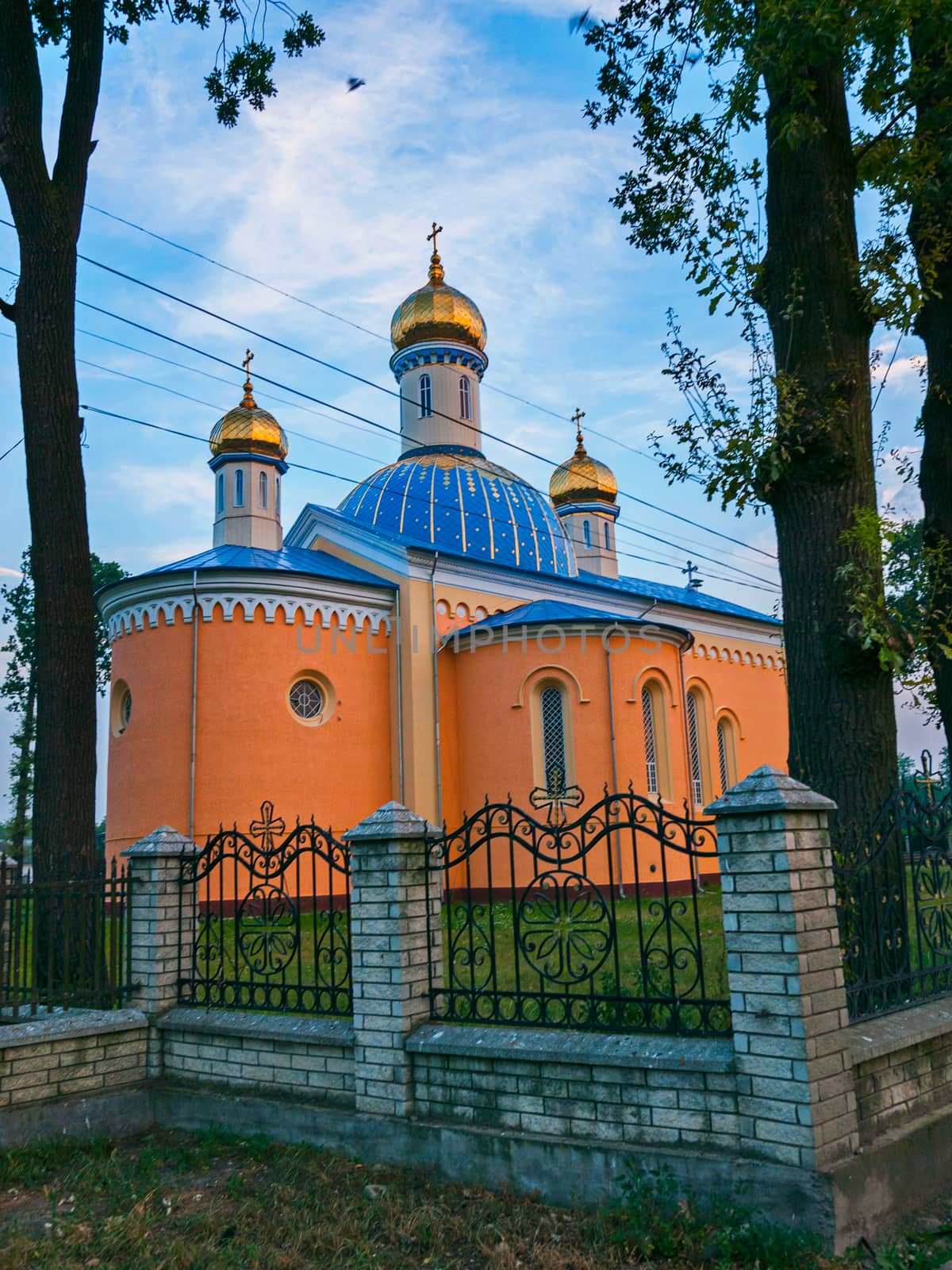Church with a blue roof and golden domes on a background of tall trees and a blue sky