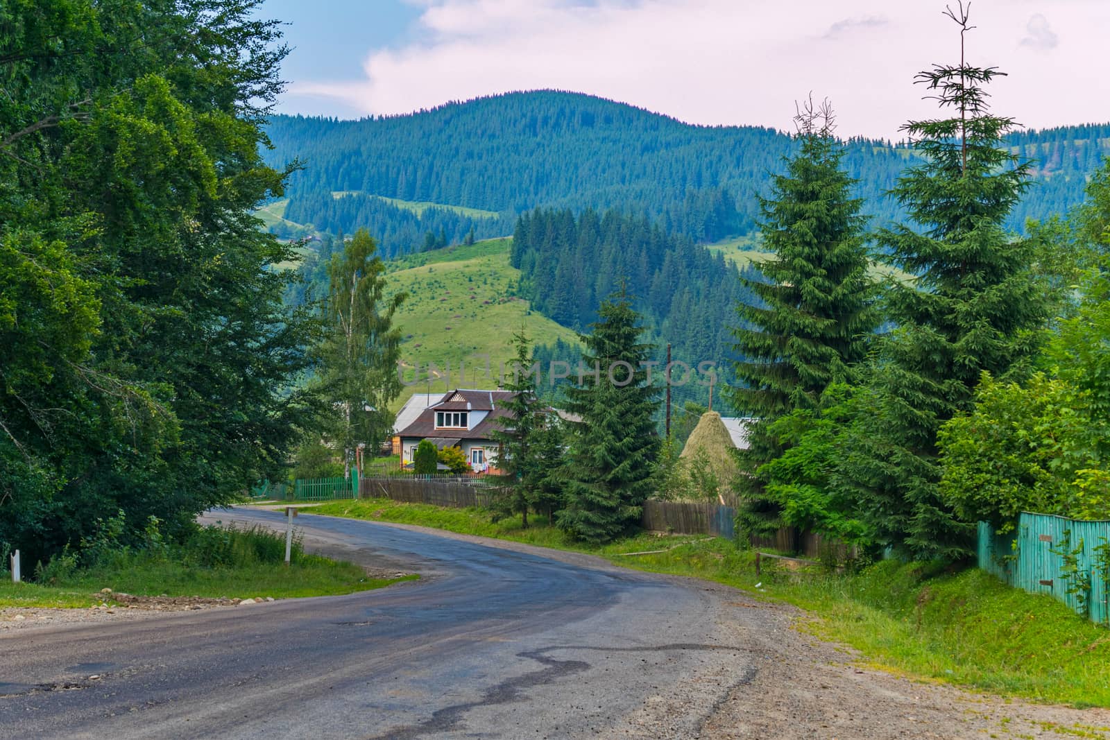 A steep winding road against the background of rural houses and huge green mountains