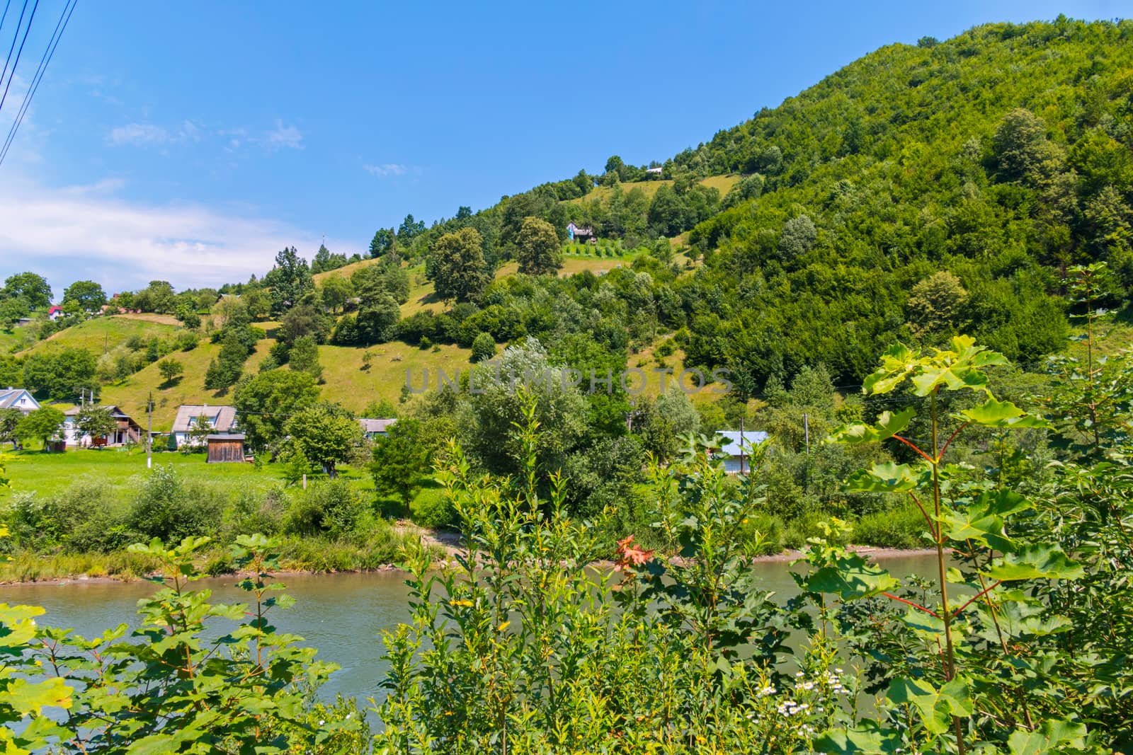 A fast, transparent river against the background of small rural houses and high green mountains