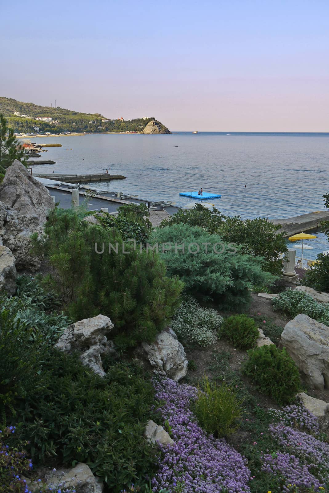 A beautiful view of the sea coast with large stones of small flowers piers coming out into the sea and seen in the distance a small rock.