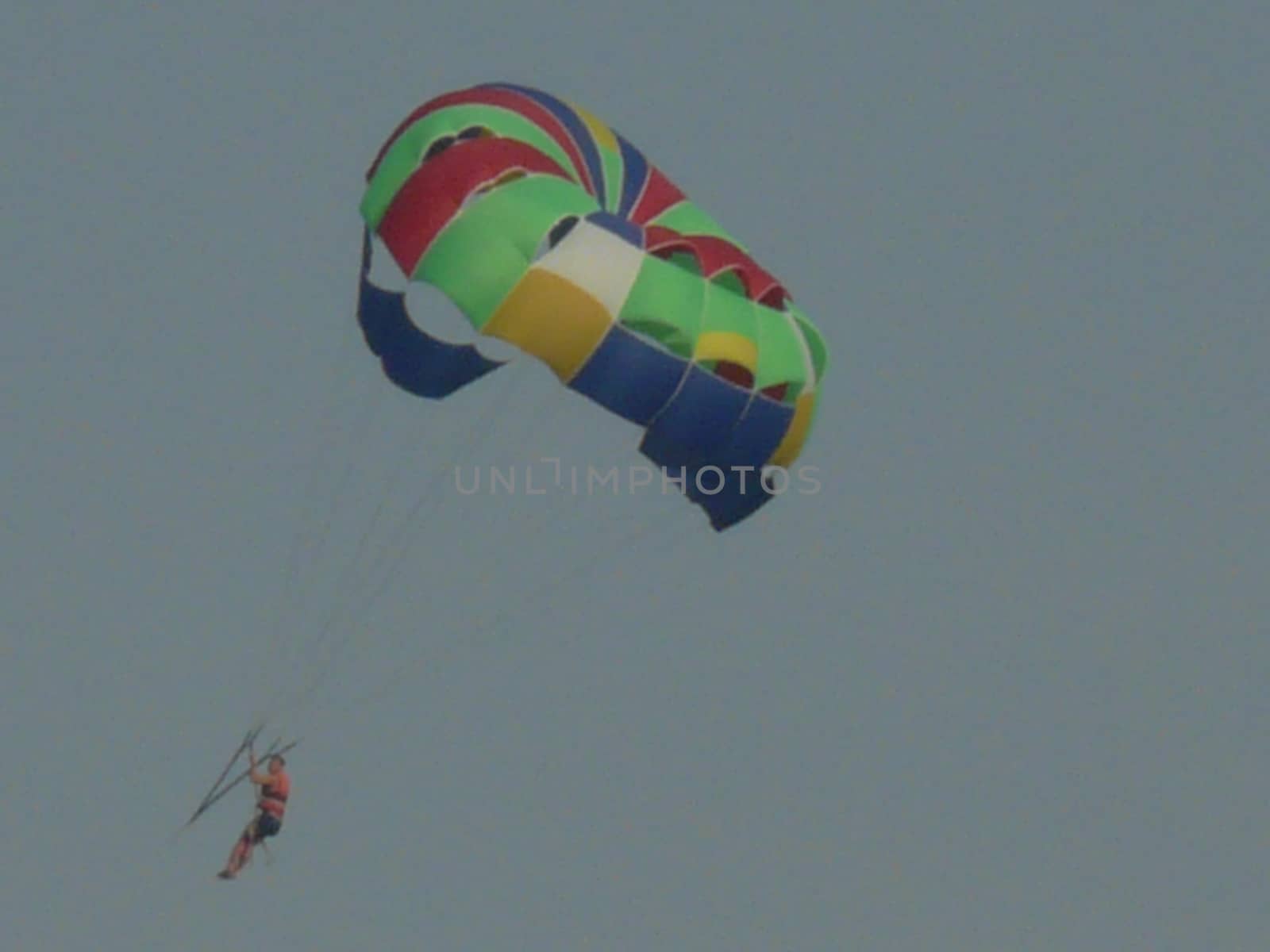 A parachutist in a blue cloudless sky hovers under a colorful dome. A good kind of rest for those who like to get a charge of vivacity and adrenaline.