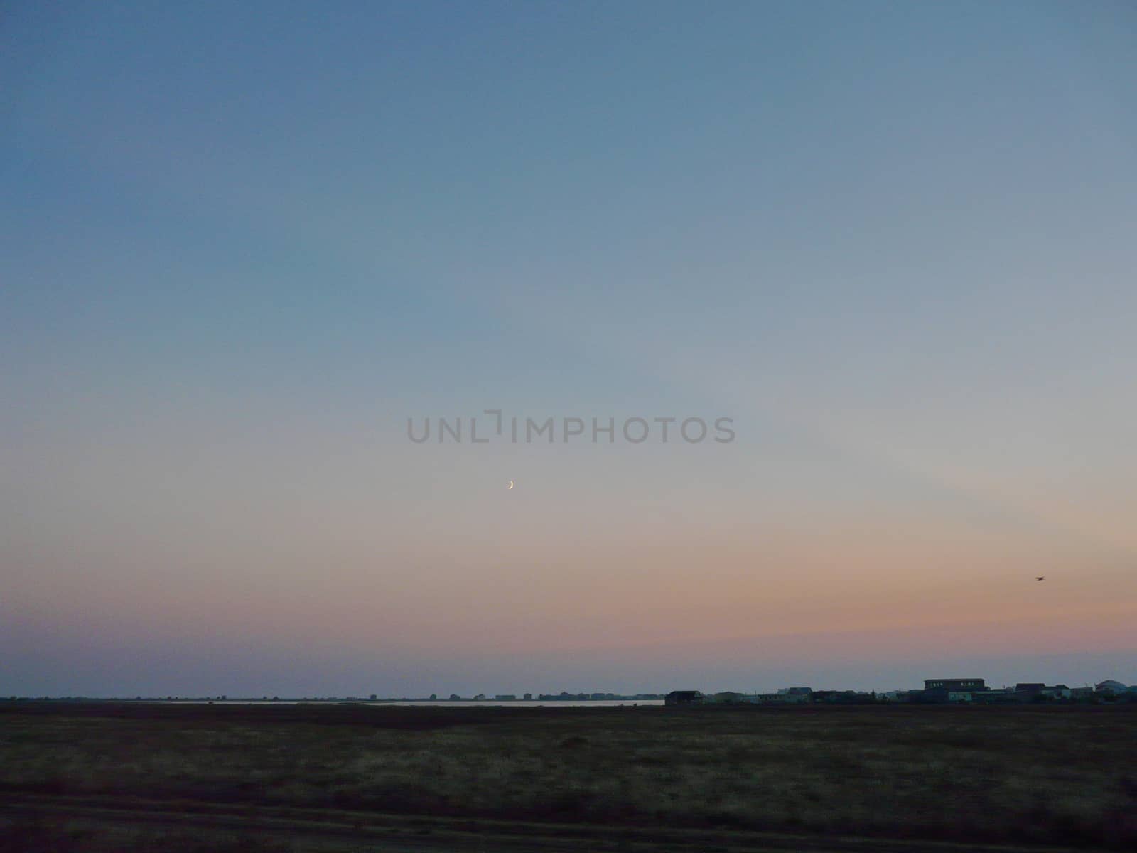 a small thin haze of the moon in a clean purple sky above the deserted spaces