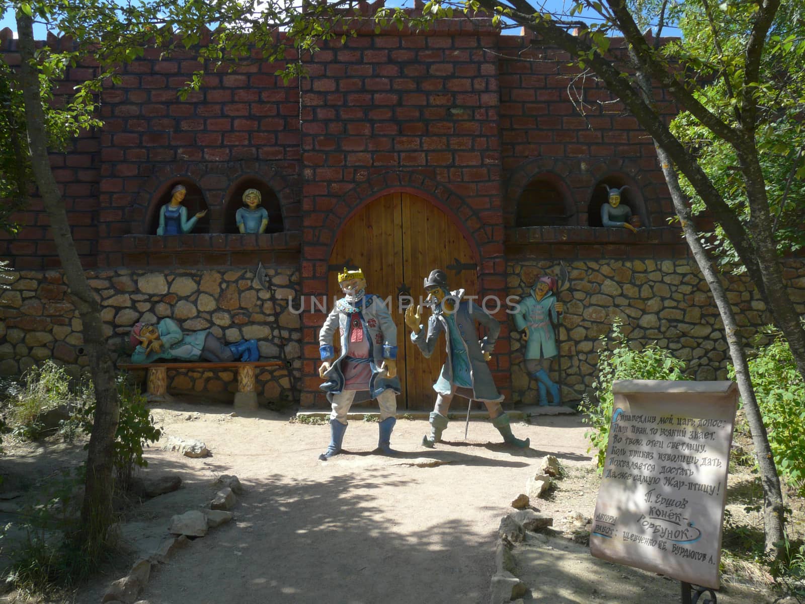 brick wall of the castle with a gate and statues in the park for tourists