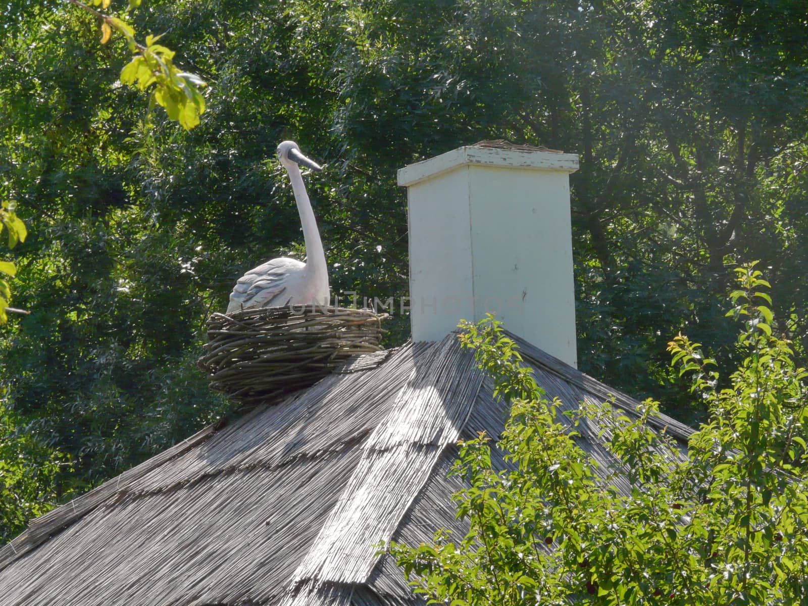 Decorative stork in a wicker nest near the smoke on the roof of the old Ukrainian house