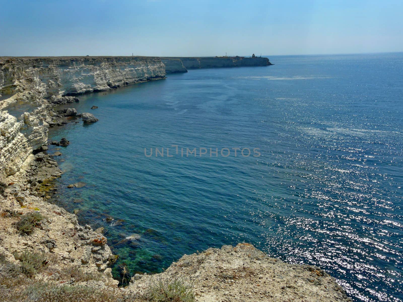A view of the sea coast with a rocky bottom and a cliff stretching along the shore with even steep walls.