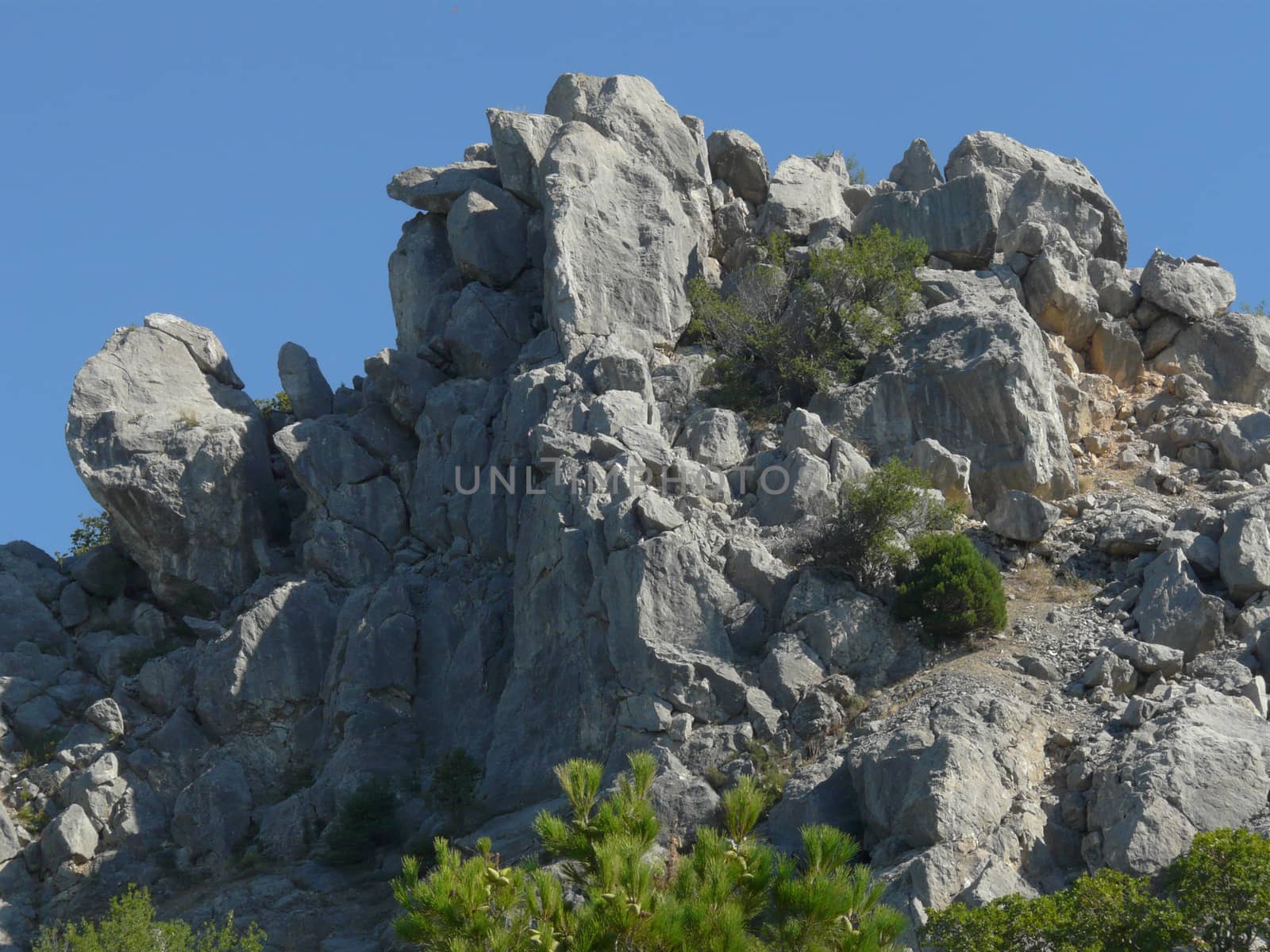 Large rocky rocky mountain with small green shrubs against the blue sky