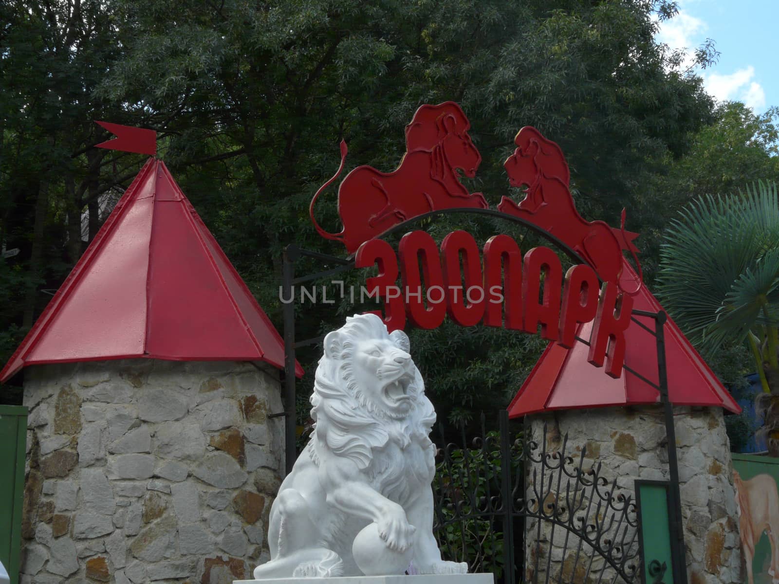 entrance to the zoo under the red inscription arch between the towers and the white lion