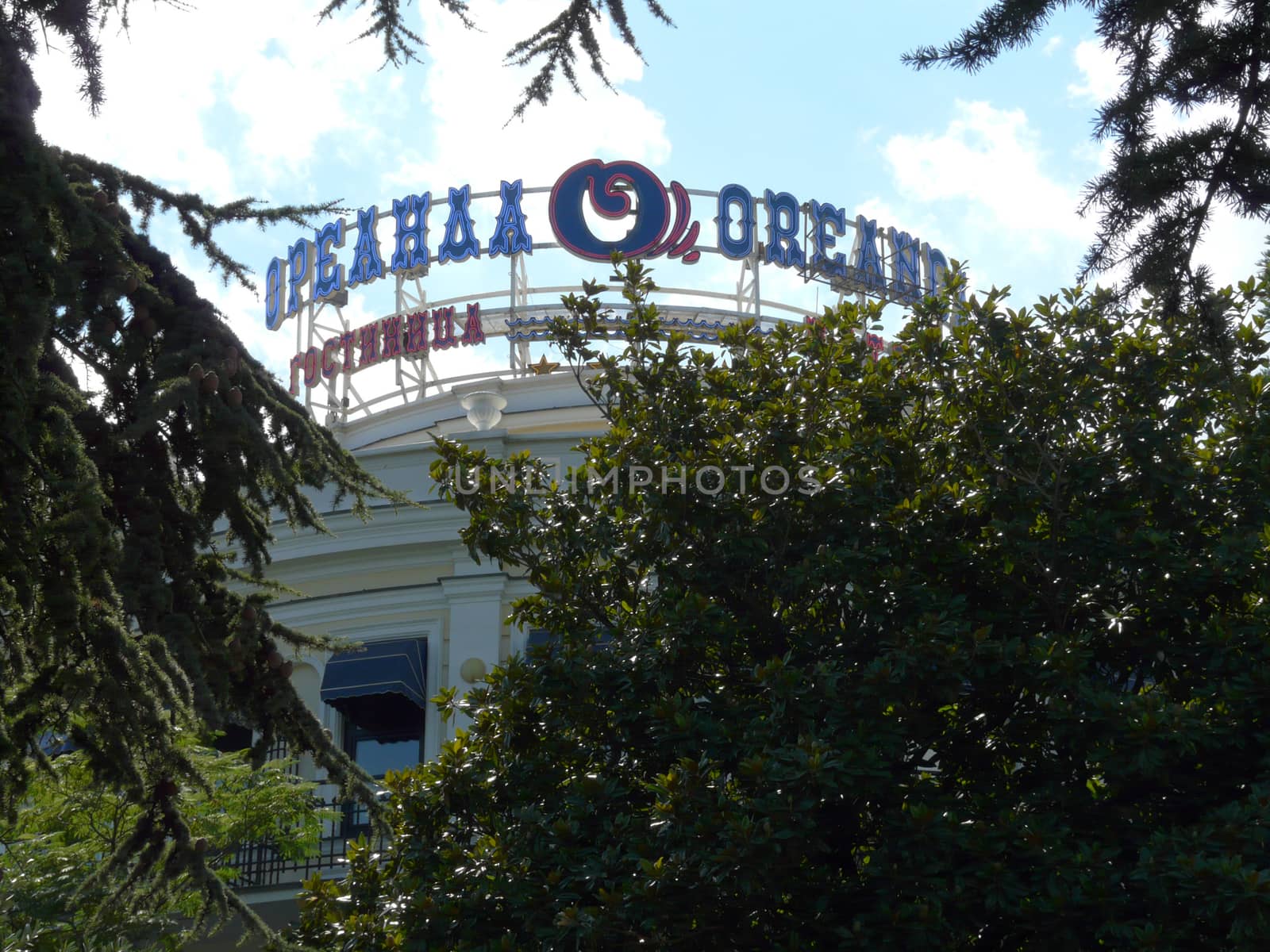 The facade of the Oreanda Hotel is seen between thick green bushes and lush trees of thick trees