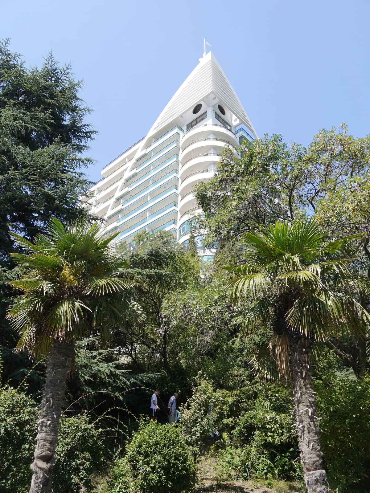 A high facade of a modern house with a chic architecture towering on green trees rising below.