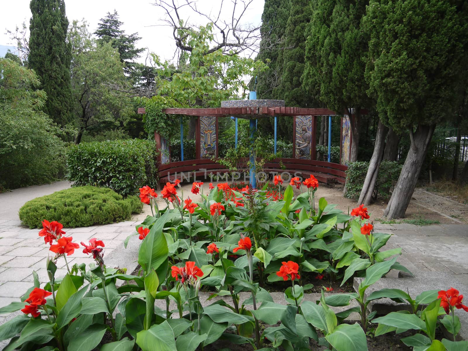 Flowerbed with beautiful red flowers on a long green stem near the semicircular gazebo