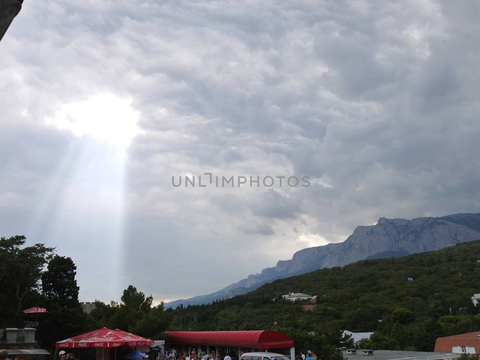 the sun's rays broke through the thick gray clouds and fall on the green mountains by Adamchuk