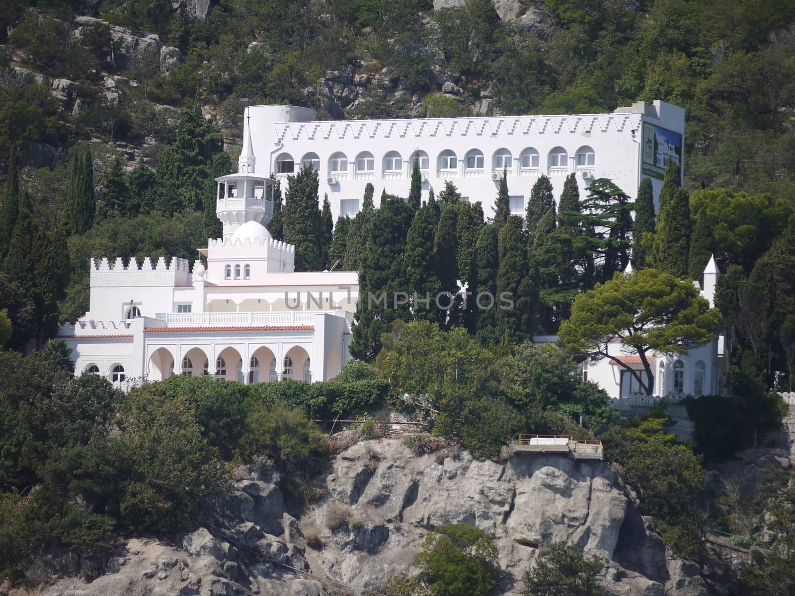 A beautiful snow-white palace with a spire on the tower is located between the greenery on the rock