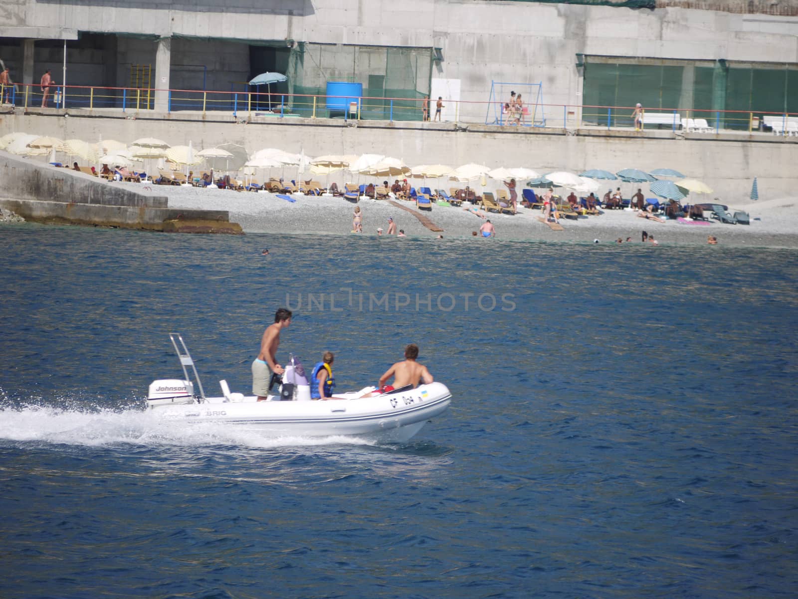 Boat sailing through the blue sea against the backdrop of a beach with a huge number of tourists