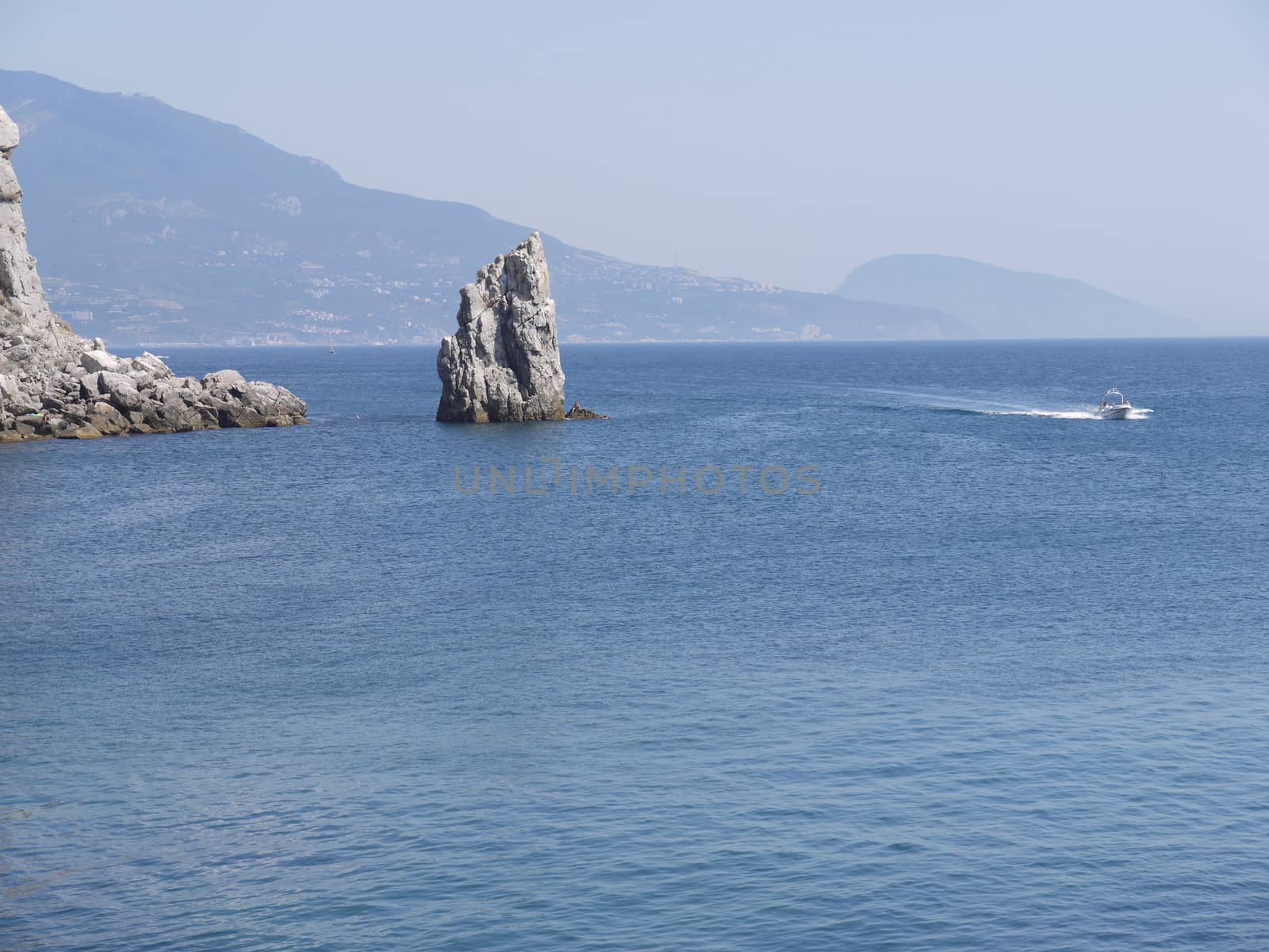 snow-white boat sailing on the flat surface of the sea water opposite the cliff