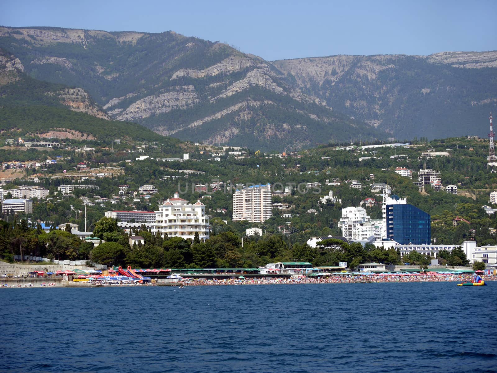 The sea beach is crammed with tourists with a beautiful view behind them to the city with a developed resort infrastructure with many hotels.