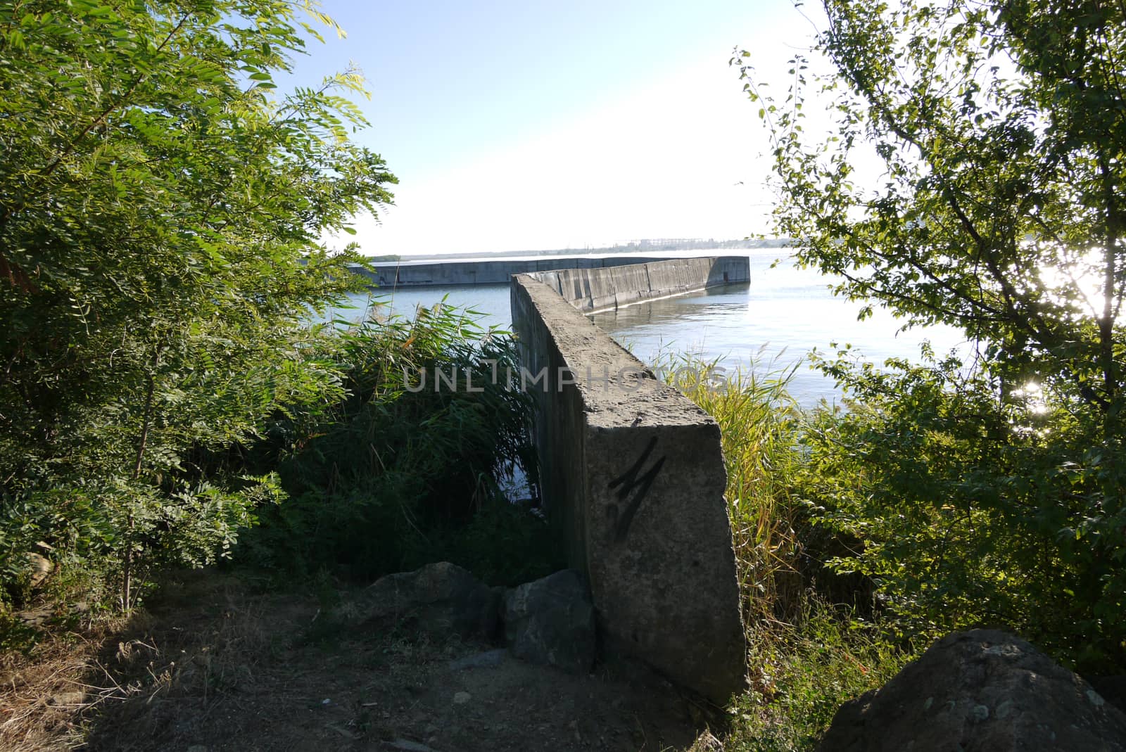 concrete fence across a pond with rocks and trees in the foreground