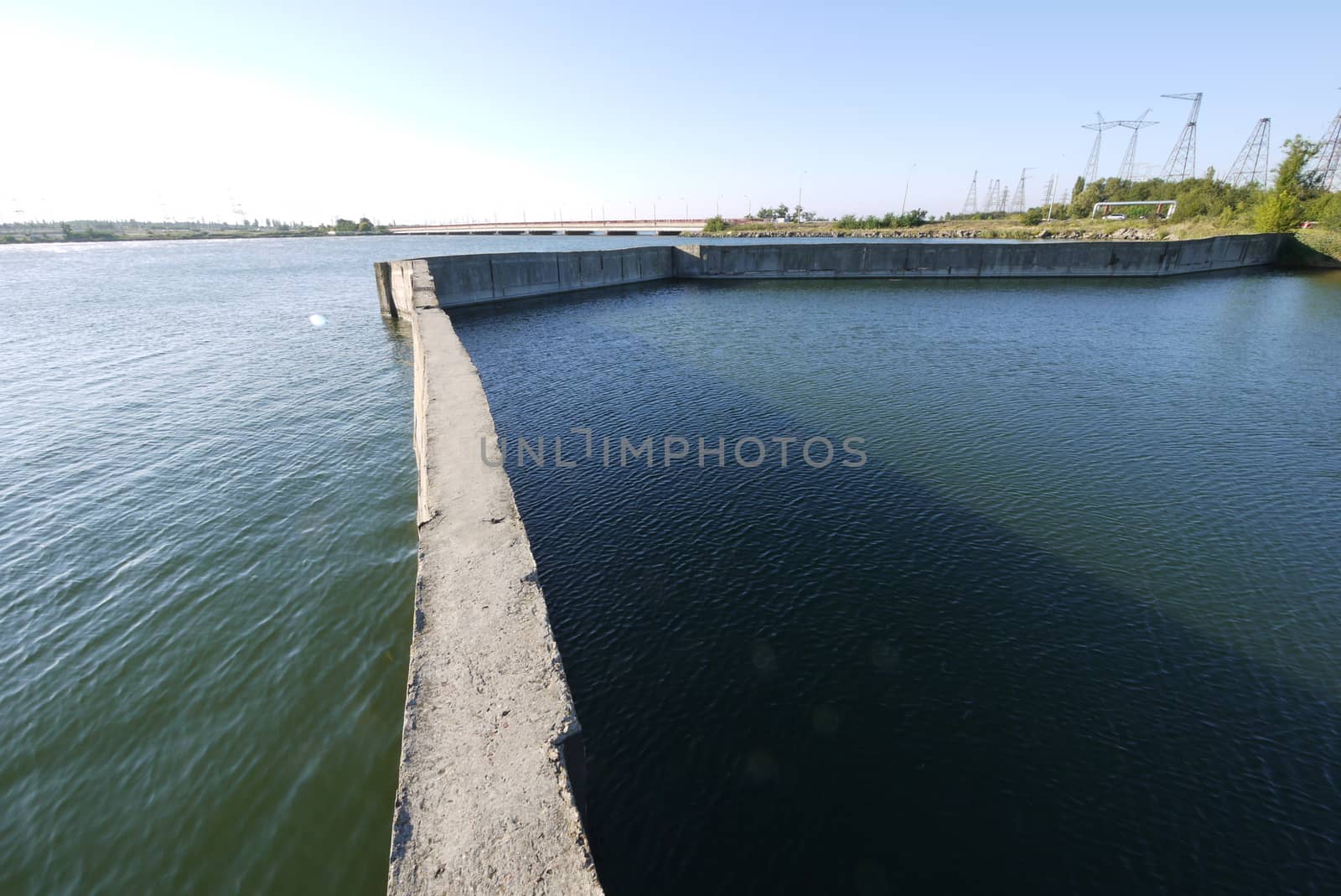 The sea bay, divided by a long concrete wall against the backdrop of a large dam