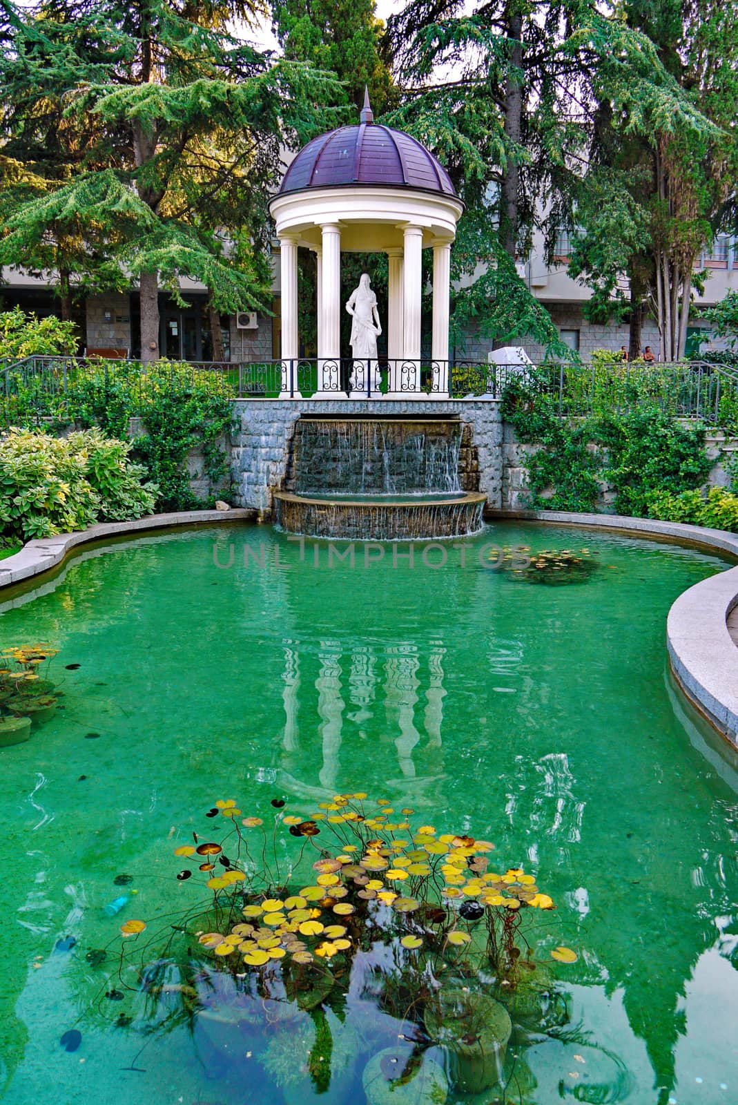 a pond with water lilies and a waterfall in the background of a gazebo