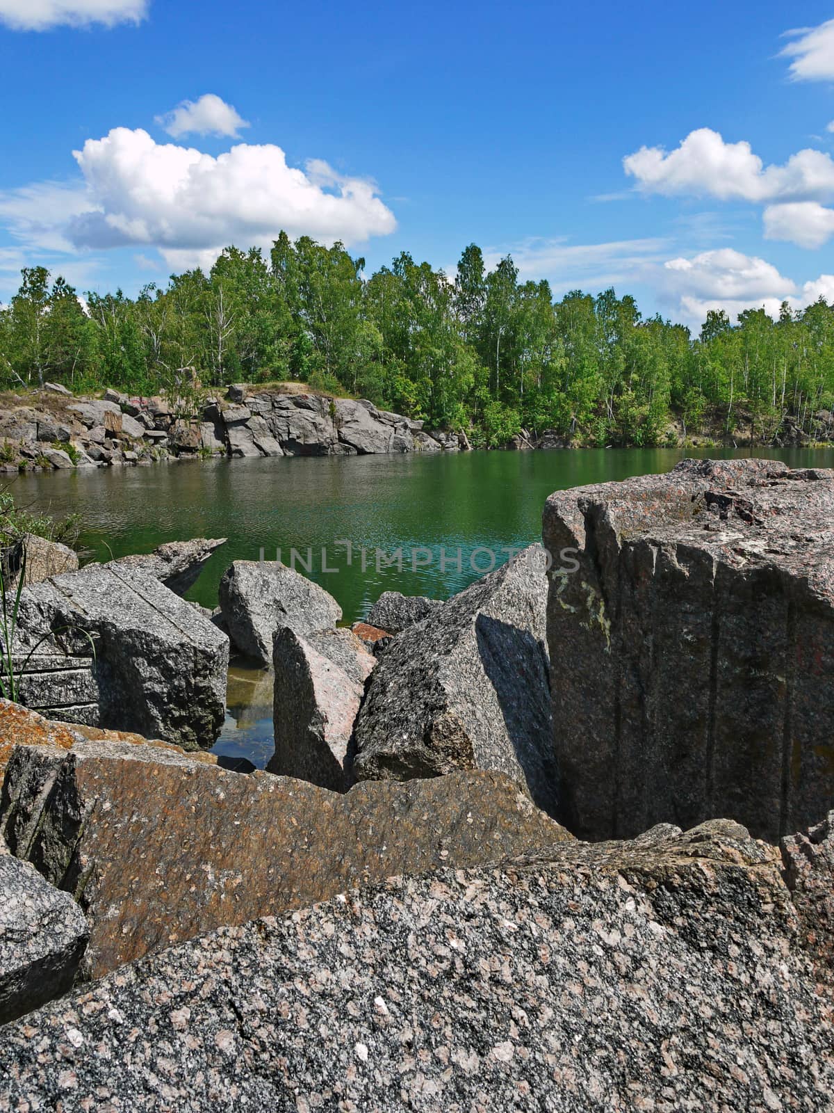 rocky shores of a lake near a forest on a background of blue sky with clouds