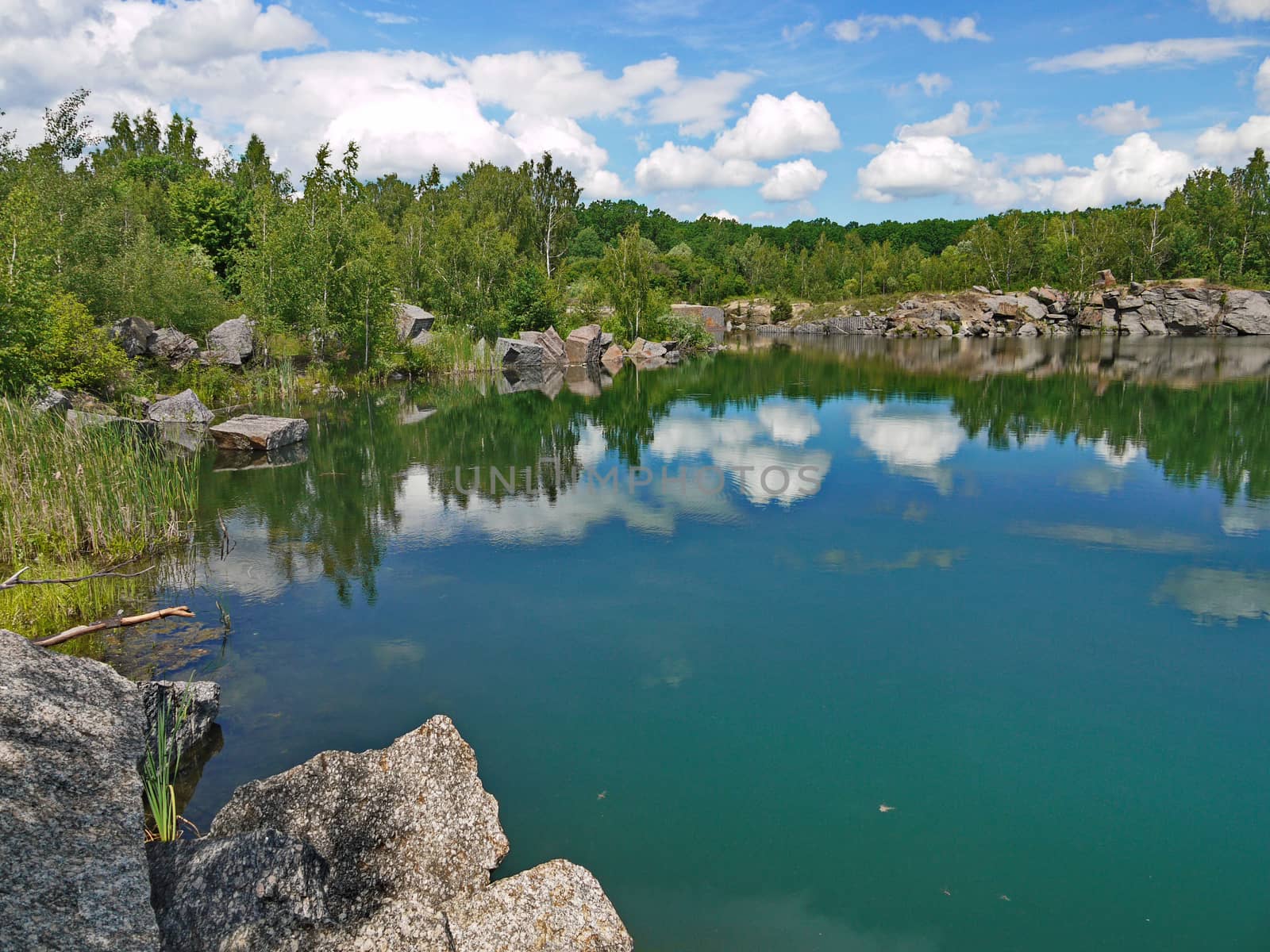 reflection of heavenly blue with clouds in the lake near the forest on the stony banks