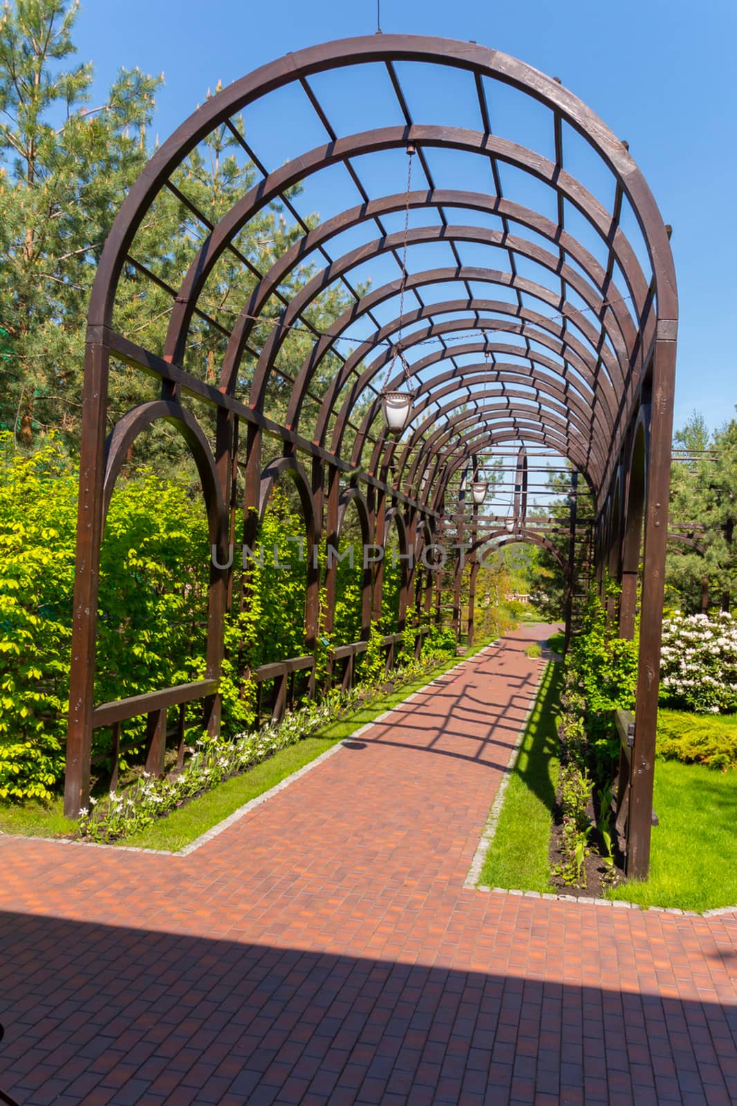 A tiled alley with a metal arch and flowers on the sides against a blue sky