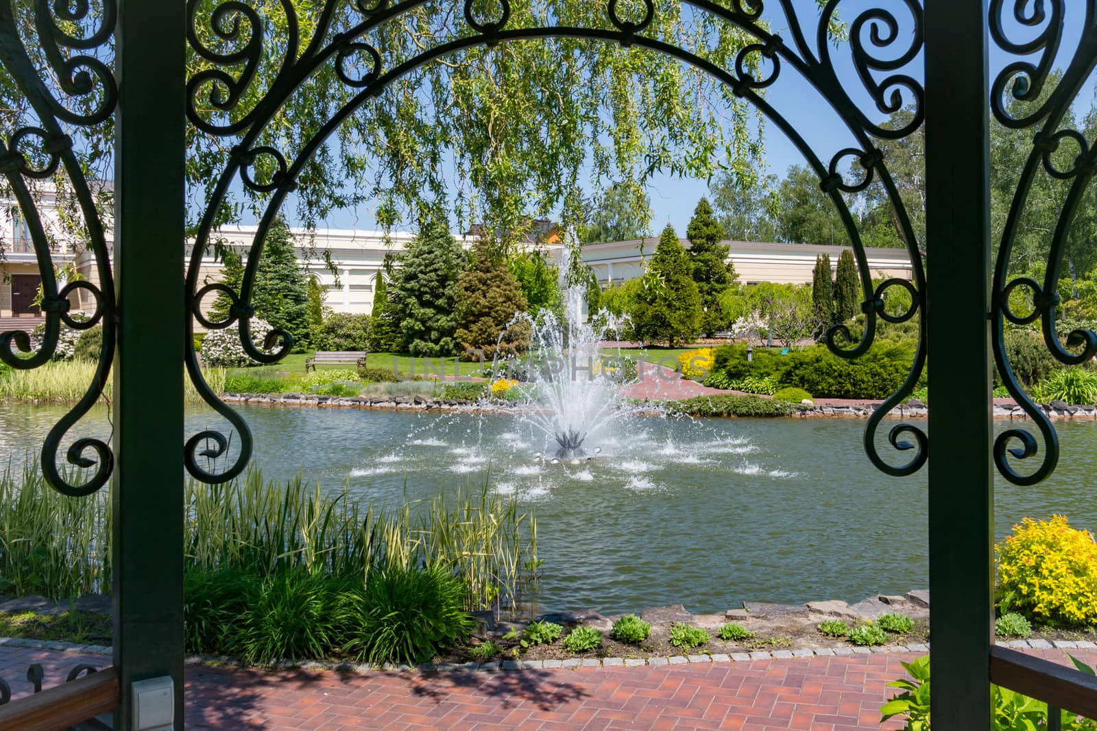 View of the fountain from under the shelter which is supported by columns with forged patterns of metal