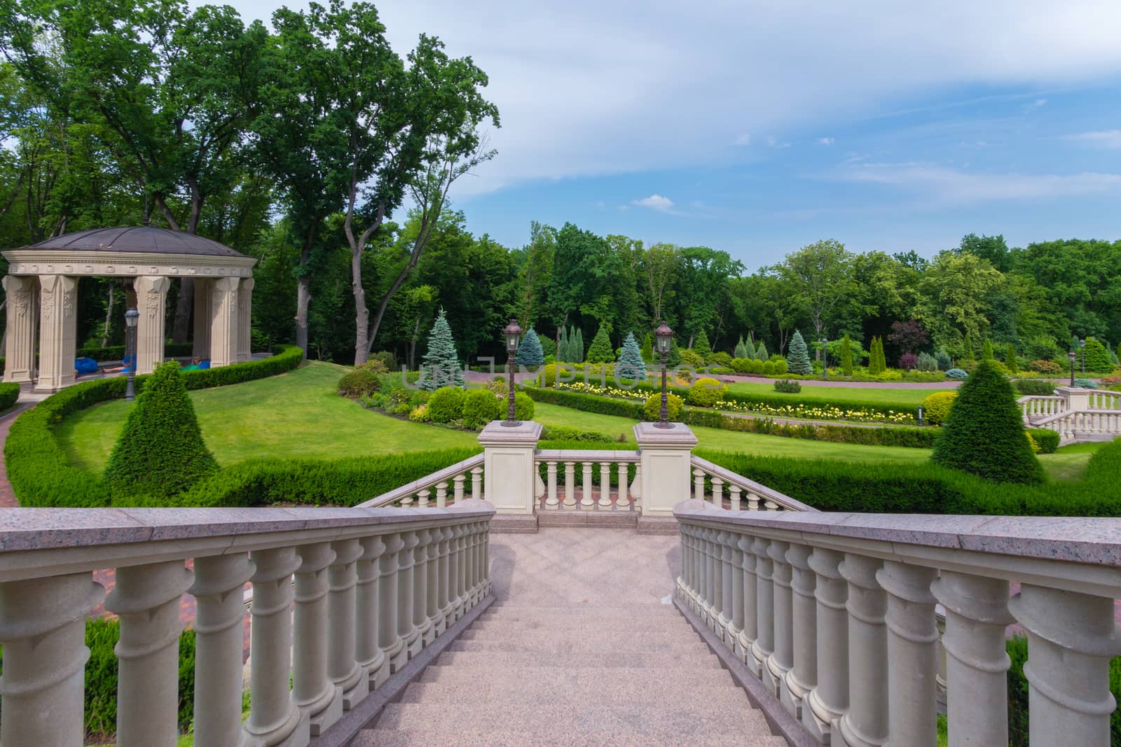 Go down to the alley of the park with crested green bushes and gazebo