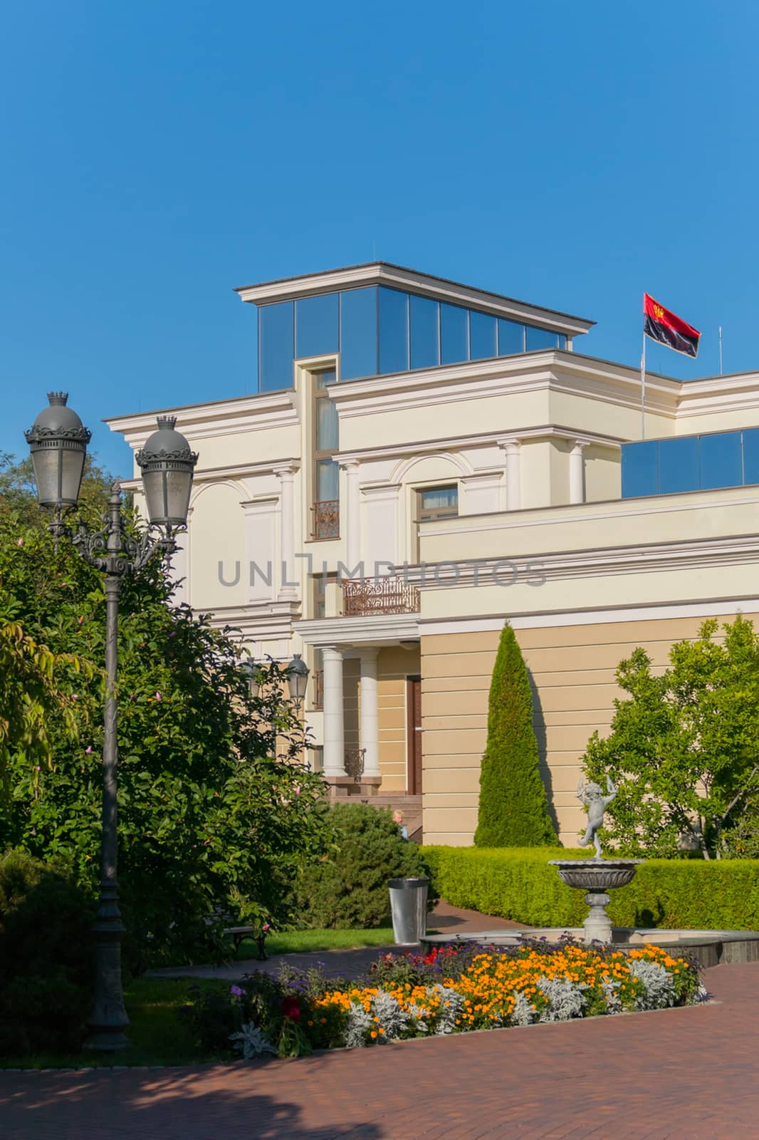 Fountain with sculpture, flower beds and ornamental trees on the background of the facade of the building