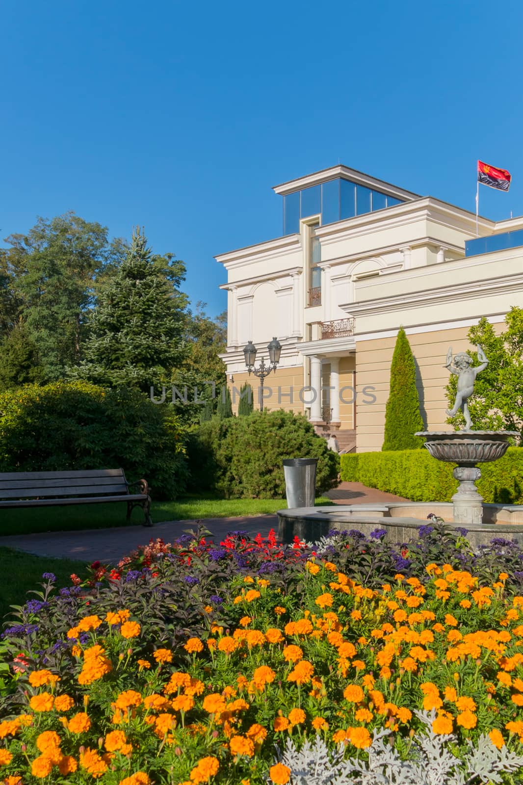 A bright flower bed around a statue in a park near a building with a track