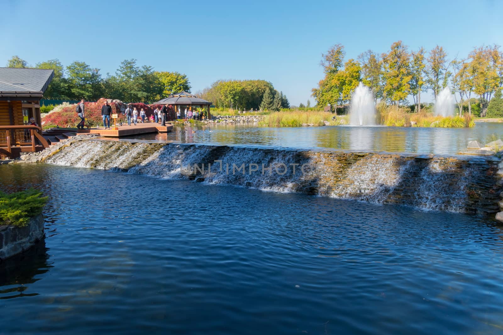 Tourists watch and photograph a small decorative waterfall flowing from one lake to another