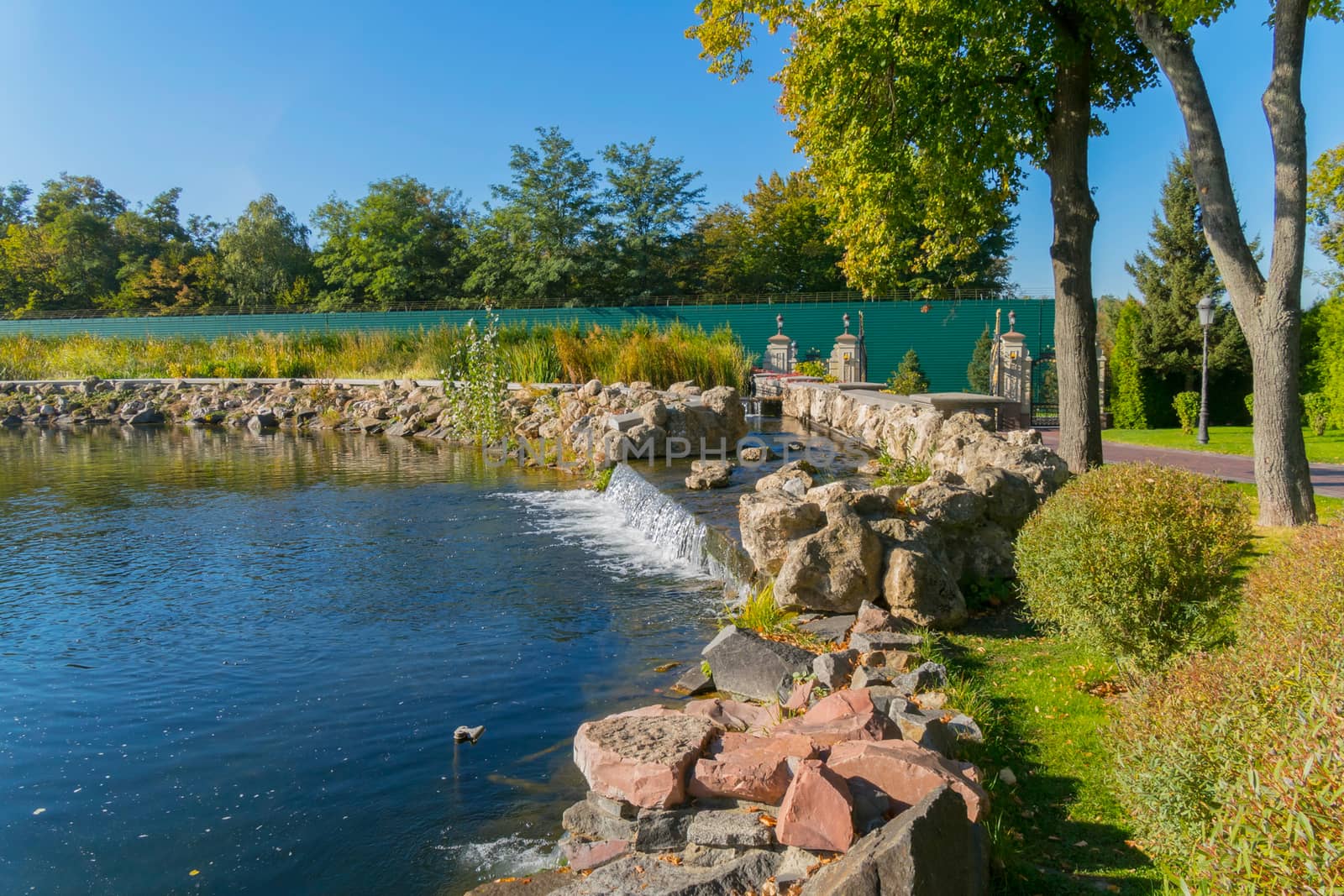 Beautiful blue transparent lake with small decorative waterfalls in the background of the park zone