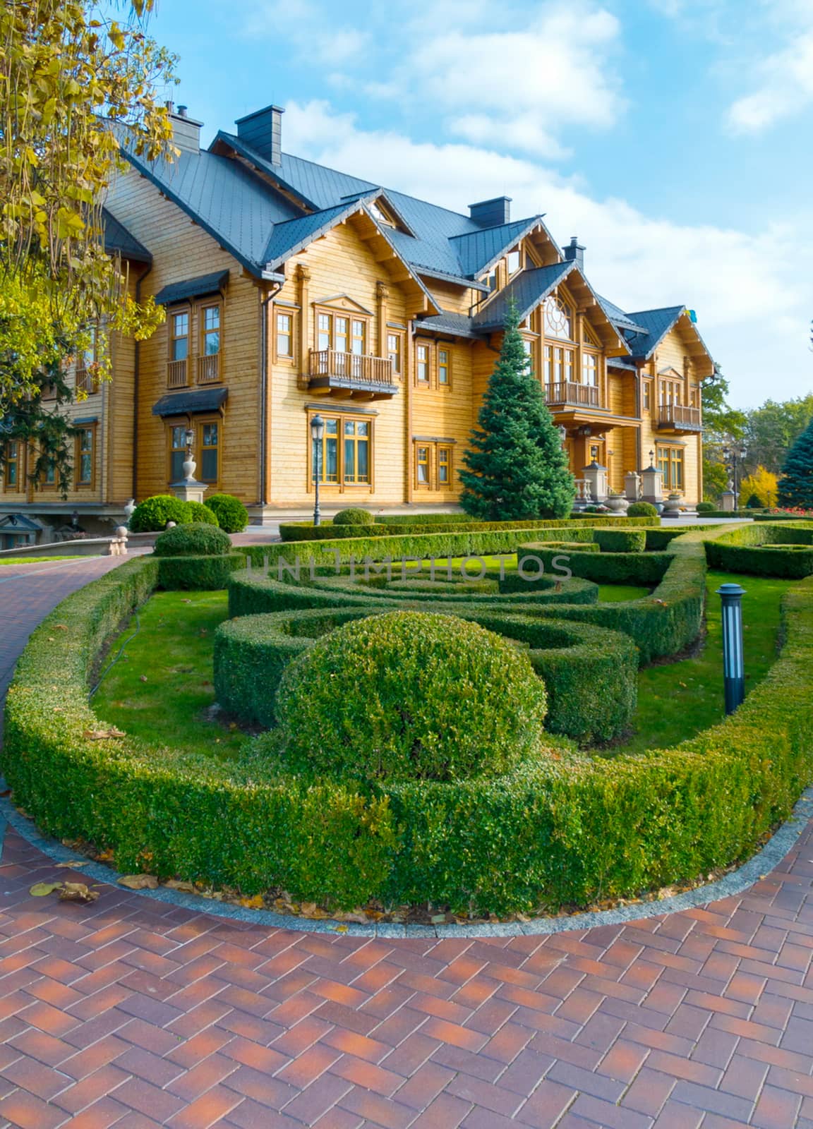 A flowerbed with a labyrinth of green bushes near the chic wooden mansion