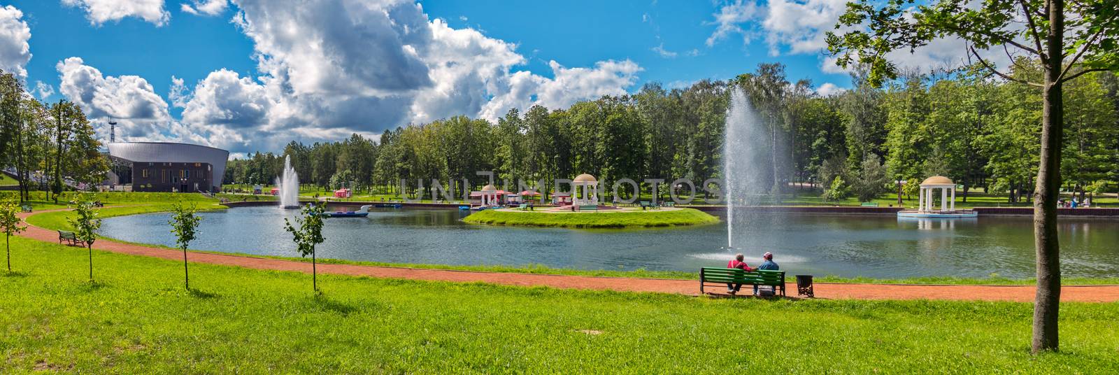 clear transparent sky slightly tightened by clouds on the background of people resting on a bench by the pond by Adamchuk