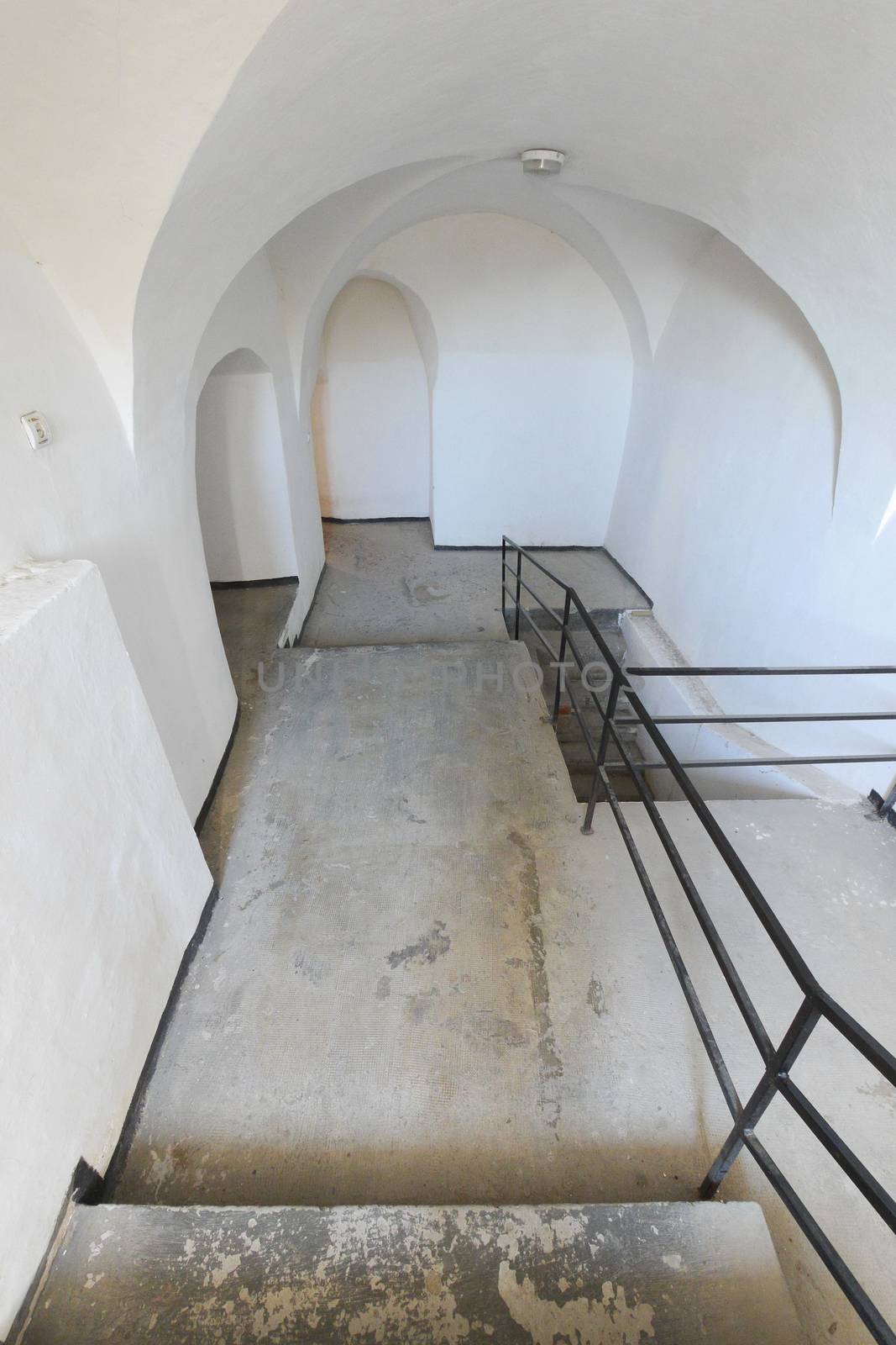 Descent with concrete steps and iron black railings against a background of white walls with rounded apertures