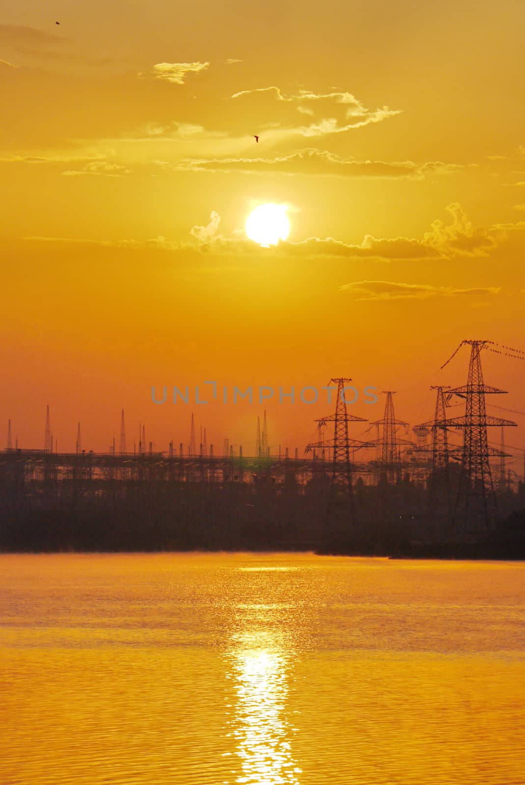 yellow sunset over the water against a power plant background