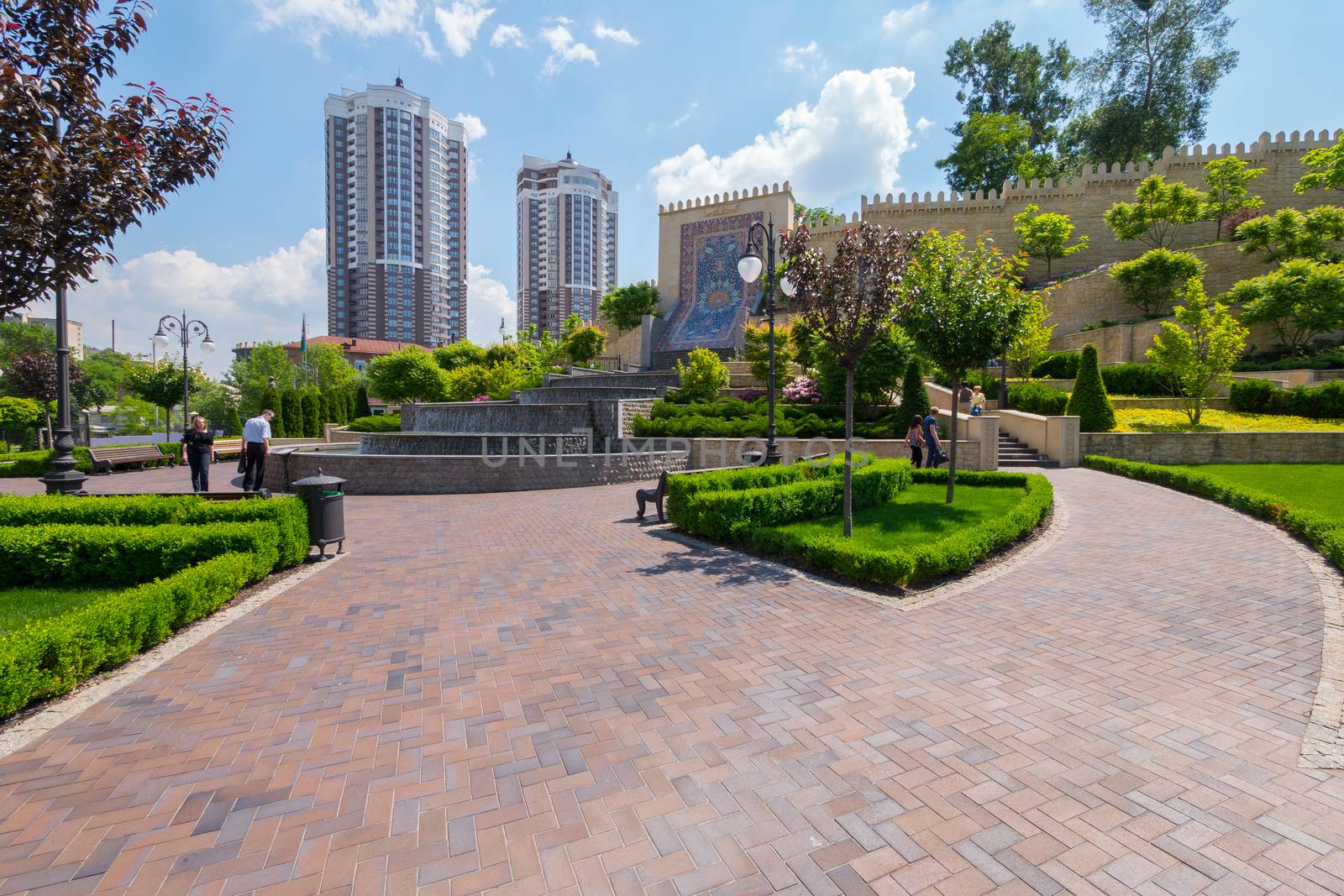 A beautiful square with a large central fountain and a historic wall on the background of tall high-rise buildings