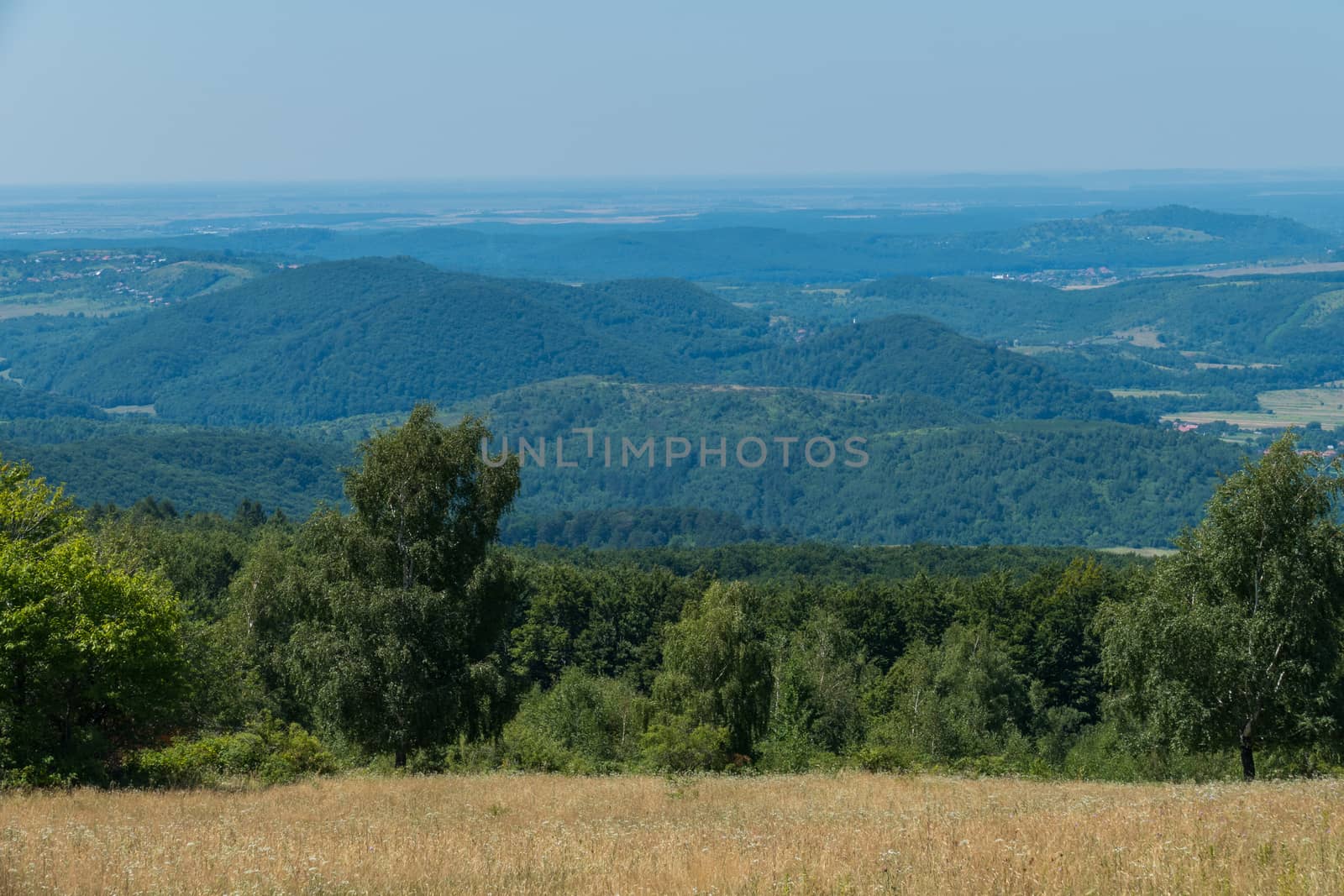 A magnificent landscape of mountainous terrain with green peaks covered with forest bright valleys stretching away to the horizon line.