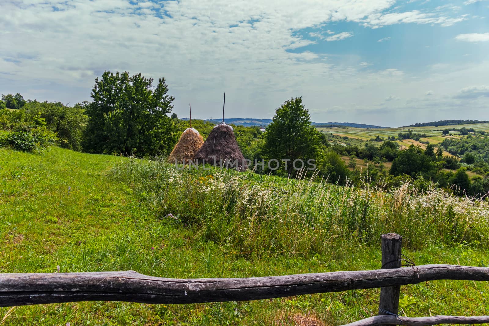 Two haystacks in a field behind a fence in the background of a beautiful sky