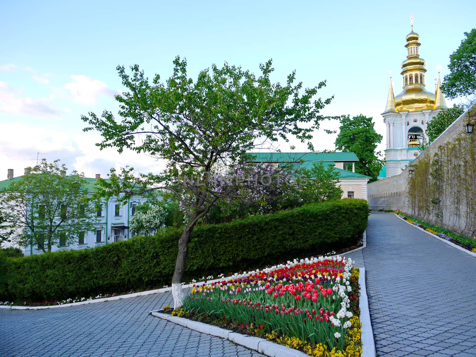 A tiled alley with a triangular flower bed full of multicolored tulips against the church church