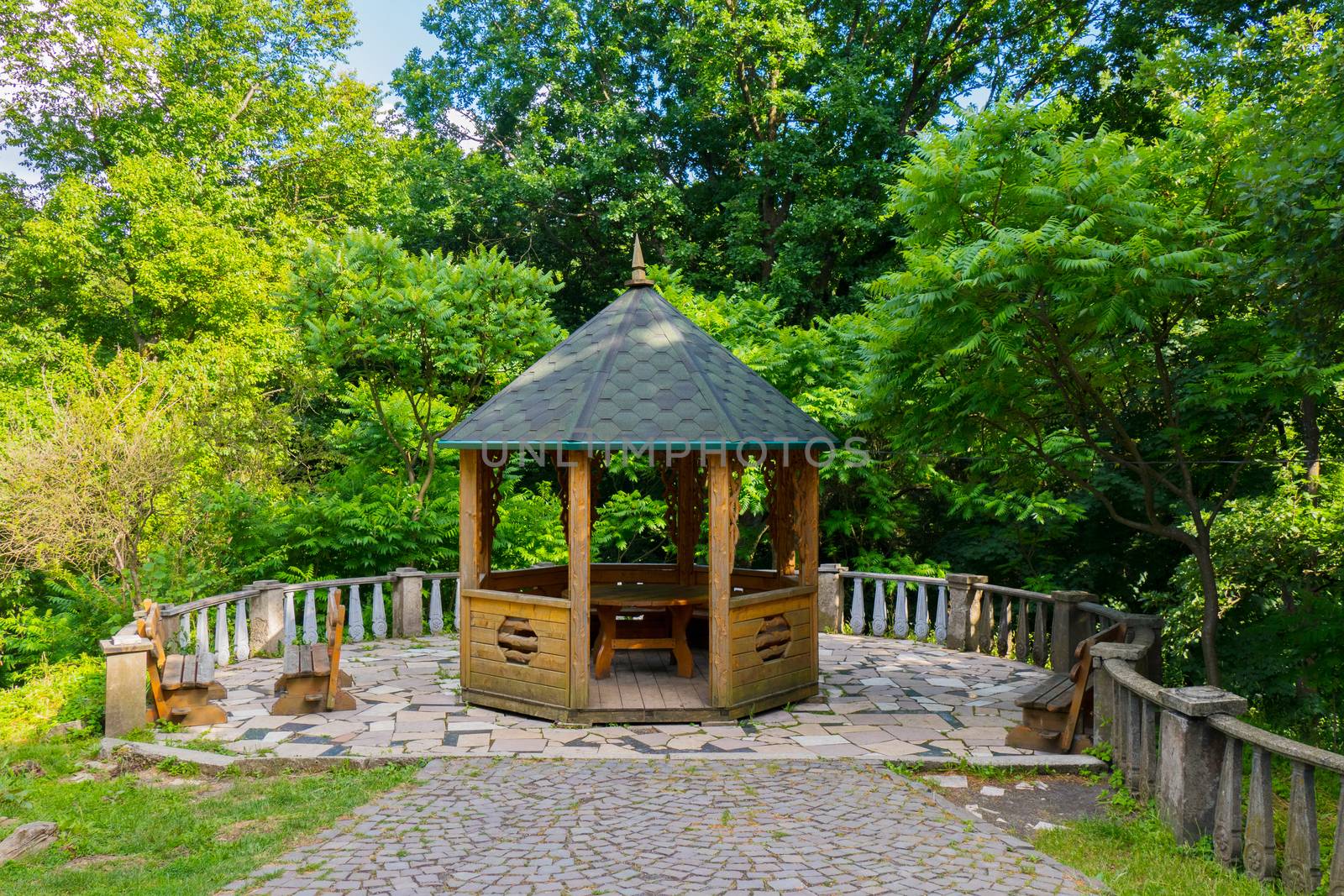 A picturesque recreation area with a wooden pergola with a green roof and benches on the sides.