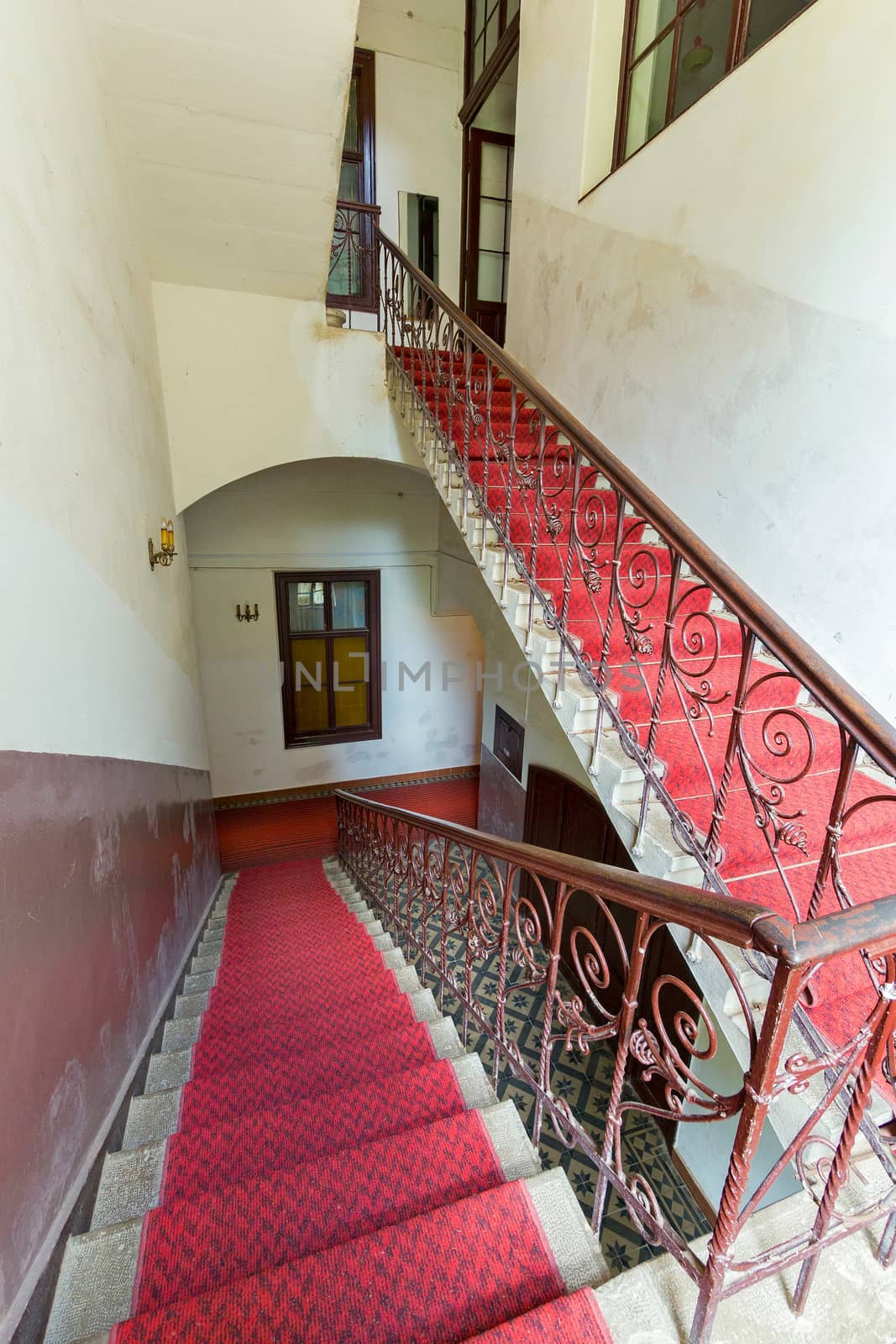 Stair flights in the building between the floors with red carpet. Painted walls and chandeliers in candlesticks on them.