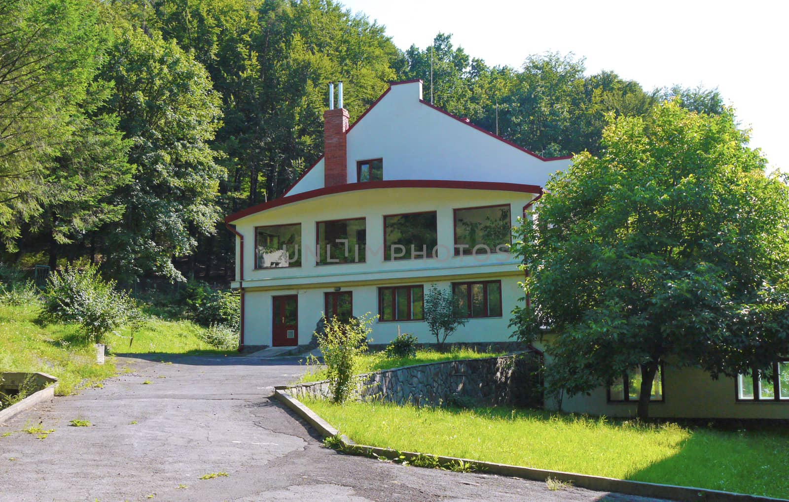a path from asphalt leading to a two-storey house with a forest growing behind it