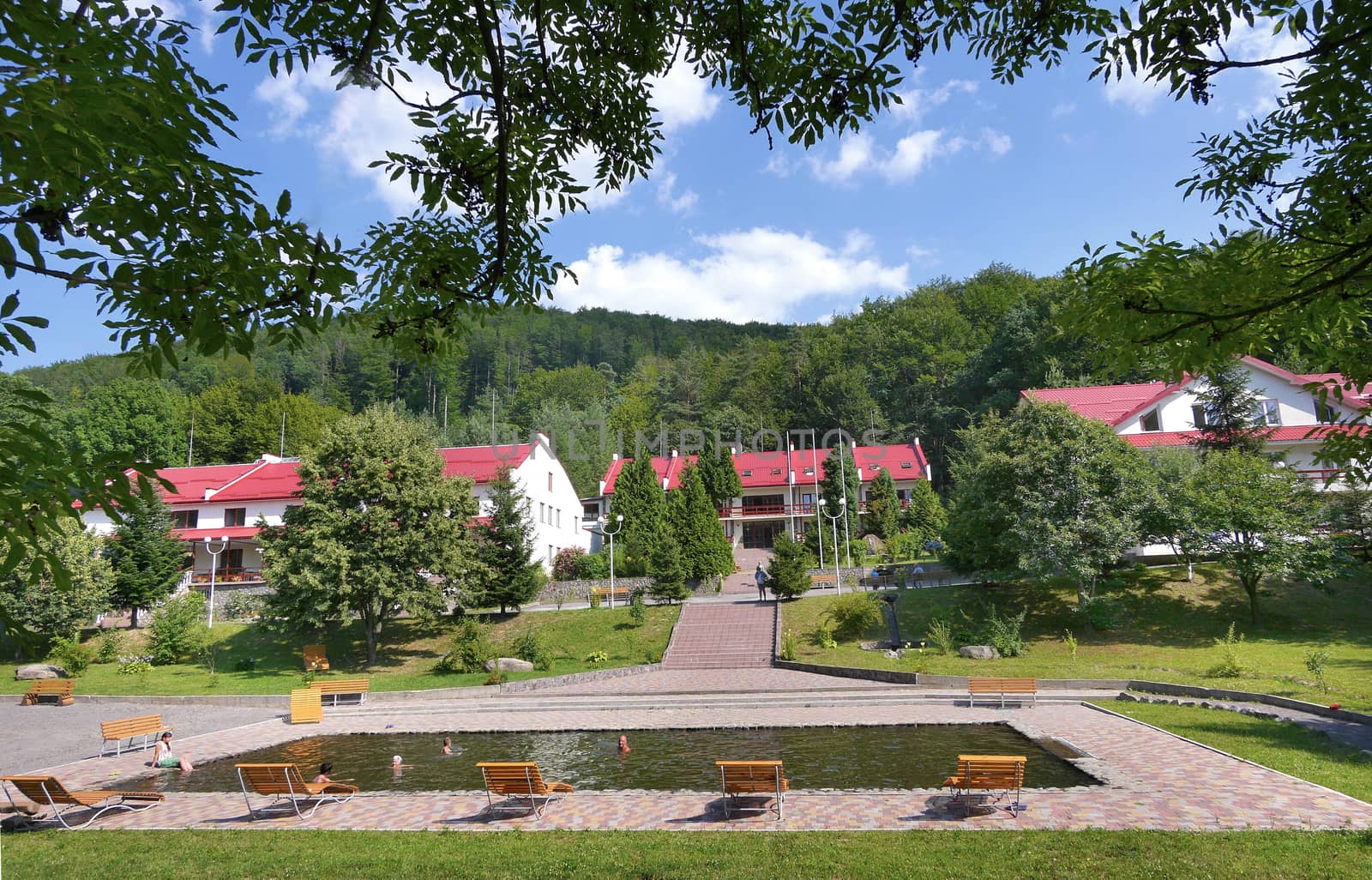 Pool with comfortable wooden sun loungers and benches in the background of the houses of the hotel complex