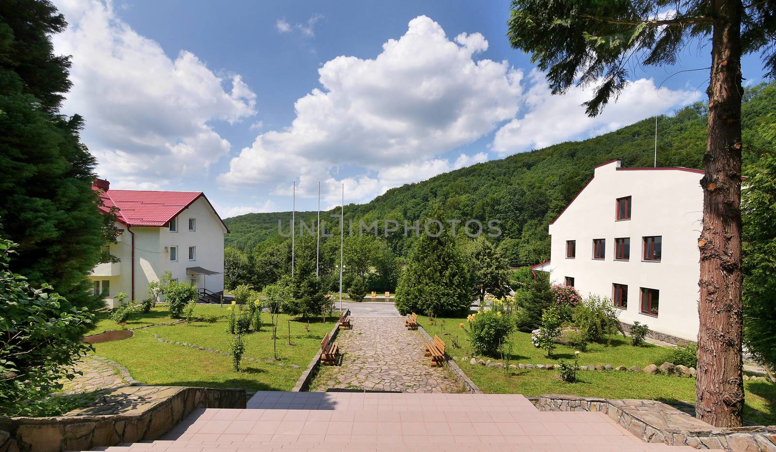 Beautiful view from the steps in the park on the green lawns growing next to houses and mountain slopes overgrown with dense forest.