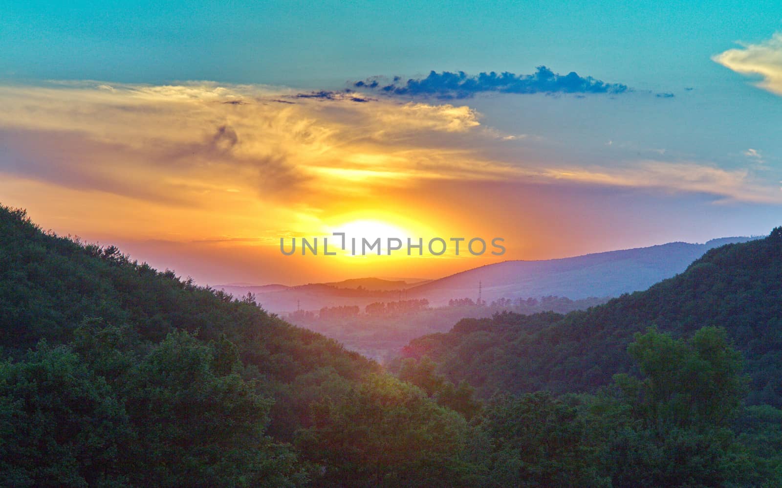 Green mountain slopes covered with thick trees against the backdrop of the beauty of the setting sun are blazing with red light illuminating the terrain on the horizon.