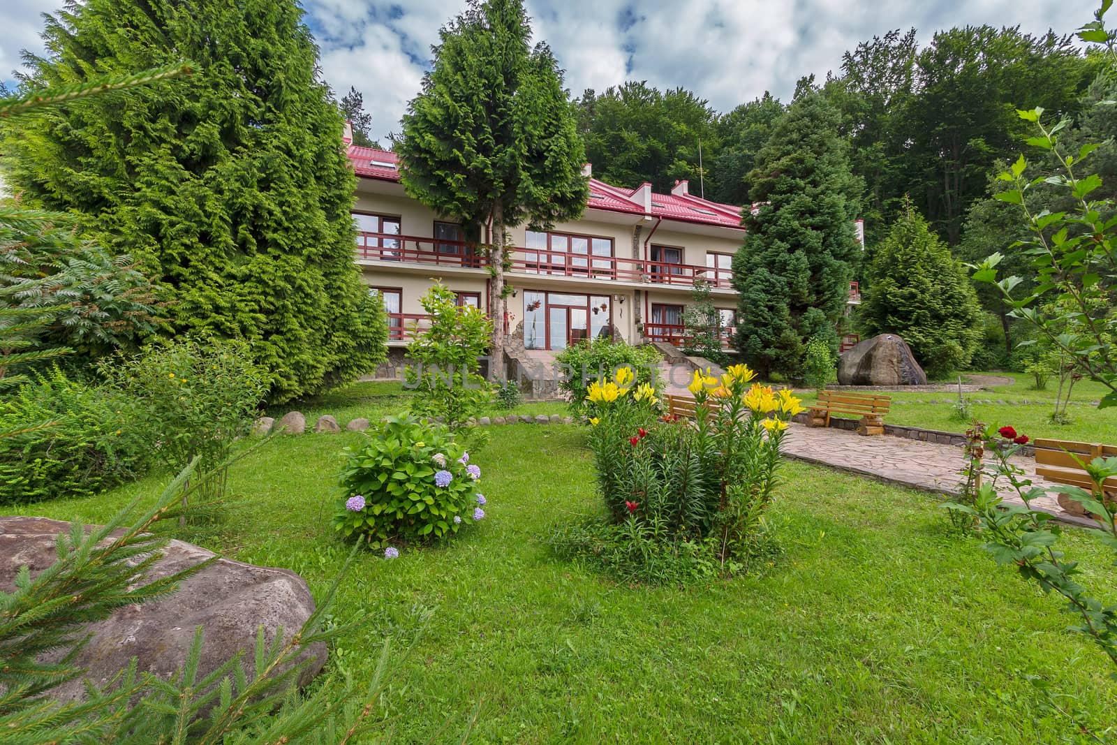 Flowerbeds with bright flowers, benches and decorative plantations on the background of a hotel complex with a red roof