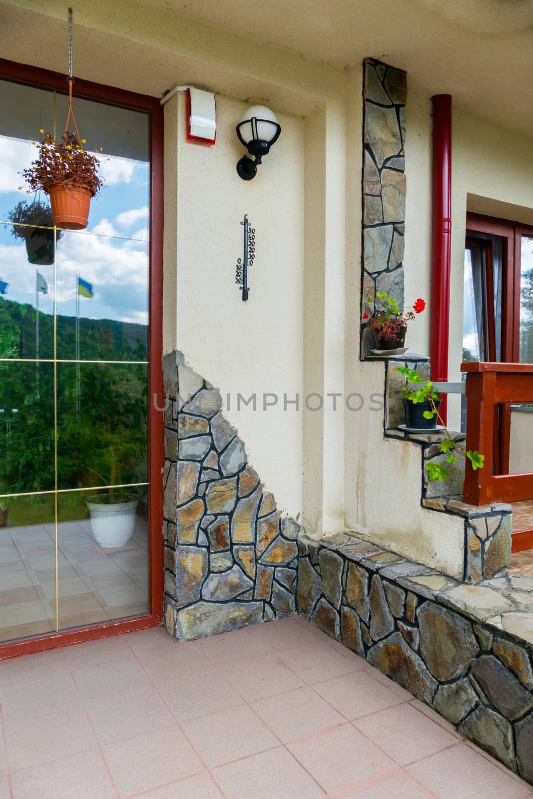 Wall with decorative masonry, forged thermometer and hanging flower vases by Adamchuk