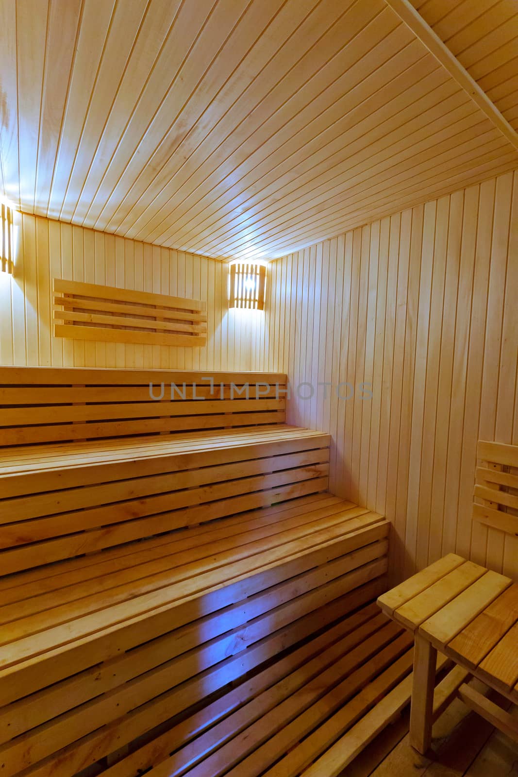 Three-tiered wooden benches with decorative lamps on the wall in a small bath